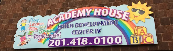 A sign for Academy House Child Development Center IV with a rainbow, sun, ABC blocks, and the phone number 201-418-0100.
