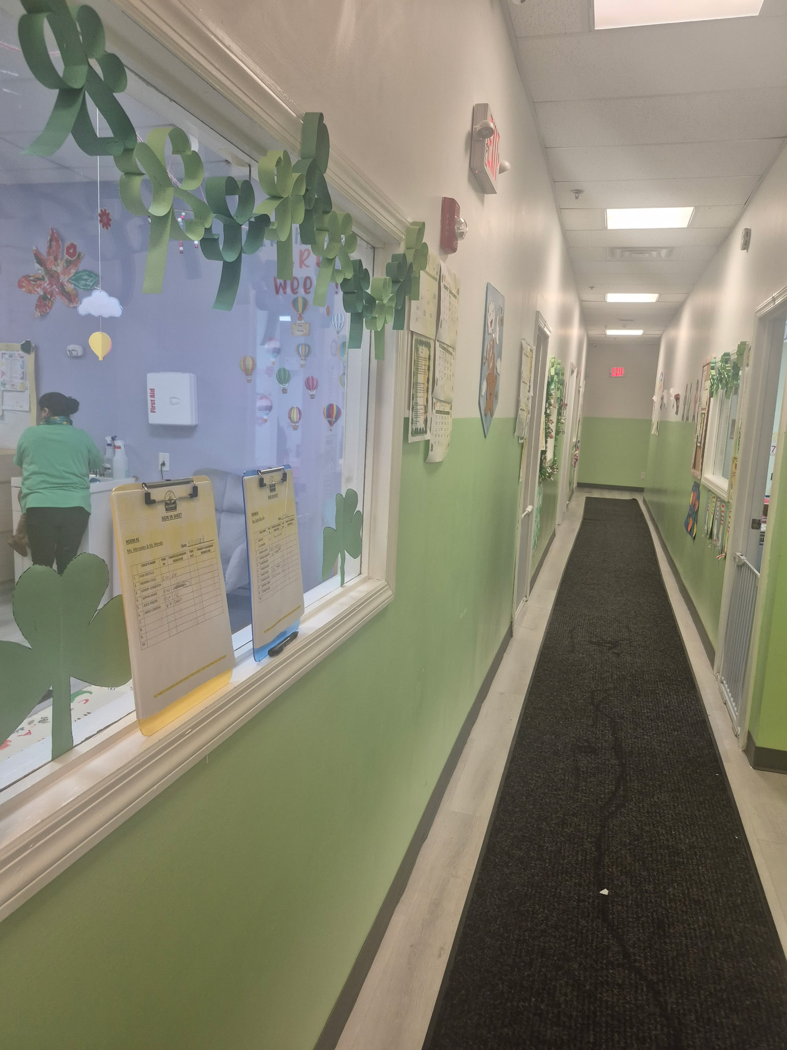 A decorated hallway with green walls and shamrock-themed decorations, featuring a black runner rug leading to a doorway.