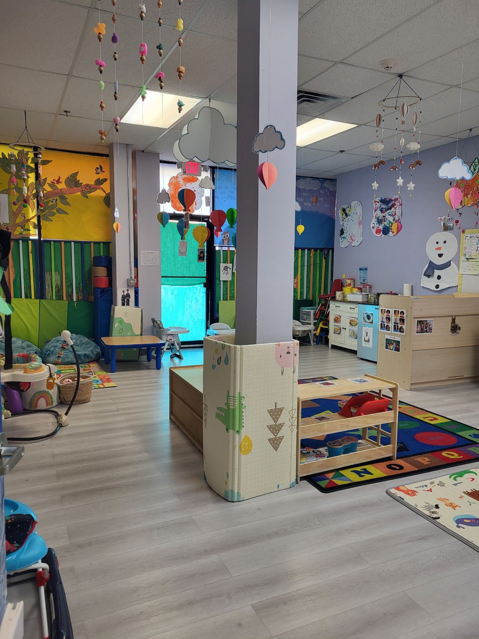 A colorful, brightly lit daycare playroom with hanging decorations, children's furniture, and a floor mat for play.