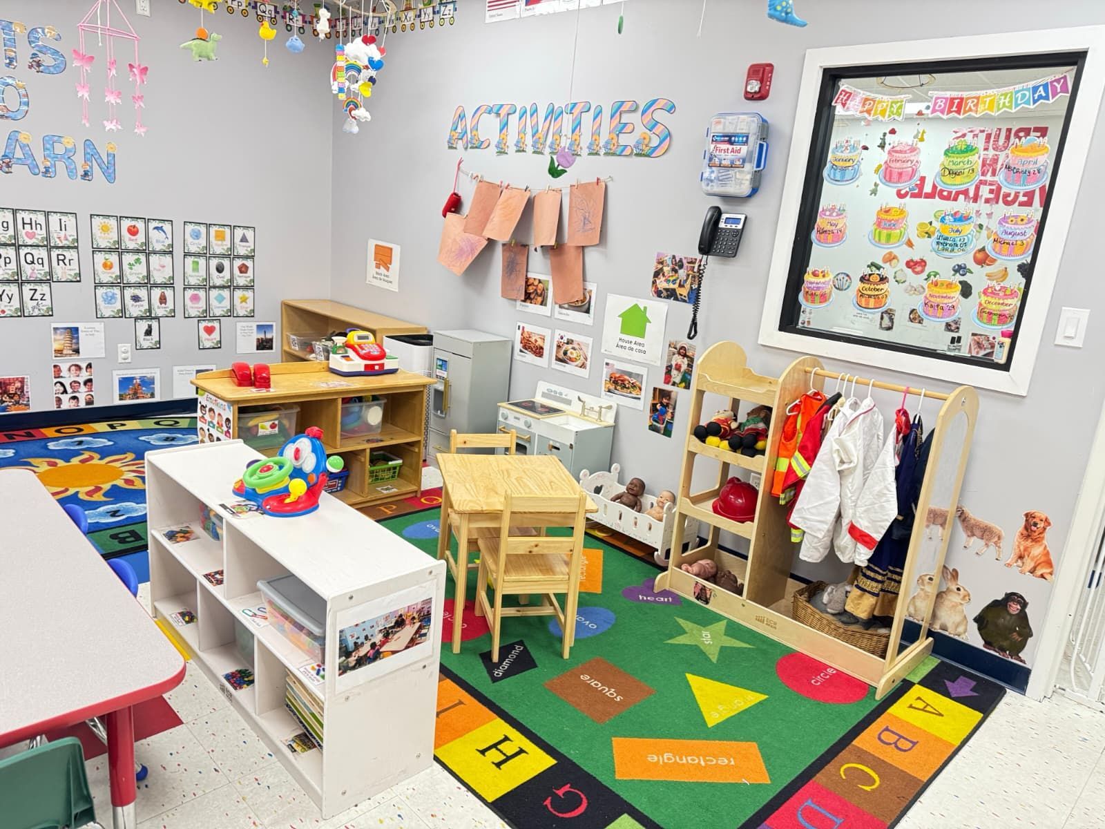 A vibrant preschool classroom featuring activity stations, wooden furniture, an alphabet rug, and wall-mounted learning aids.