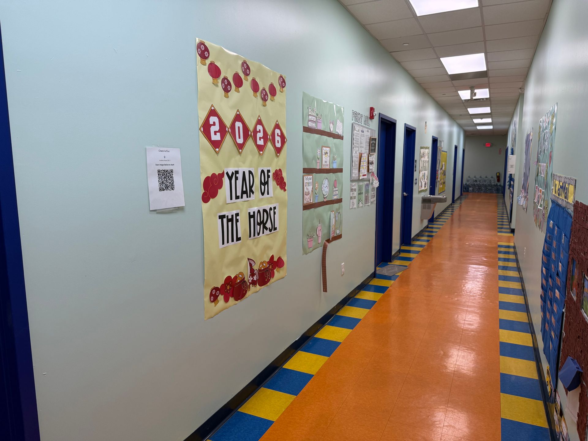 A hallway with light blue walls, orange and blue striped flooring, and posters including a 