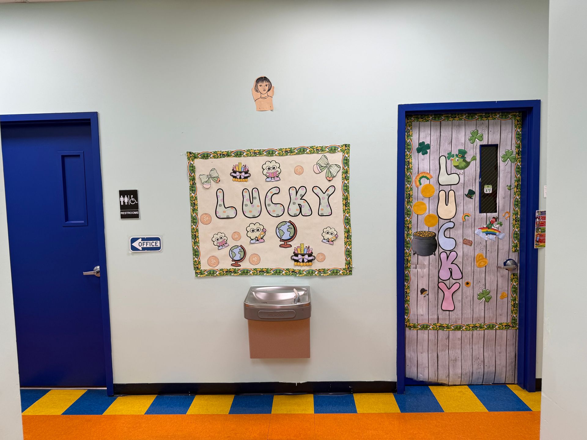 A hallway with two blue doors, a water fountain, and a St. Patrick's-themed 