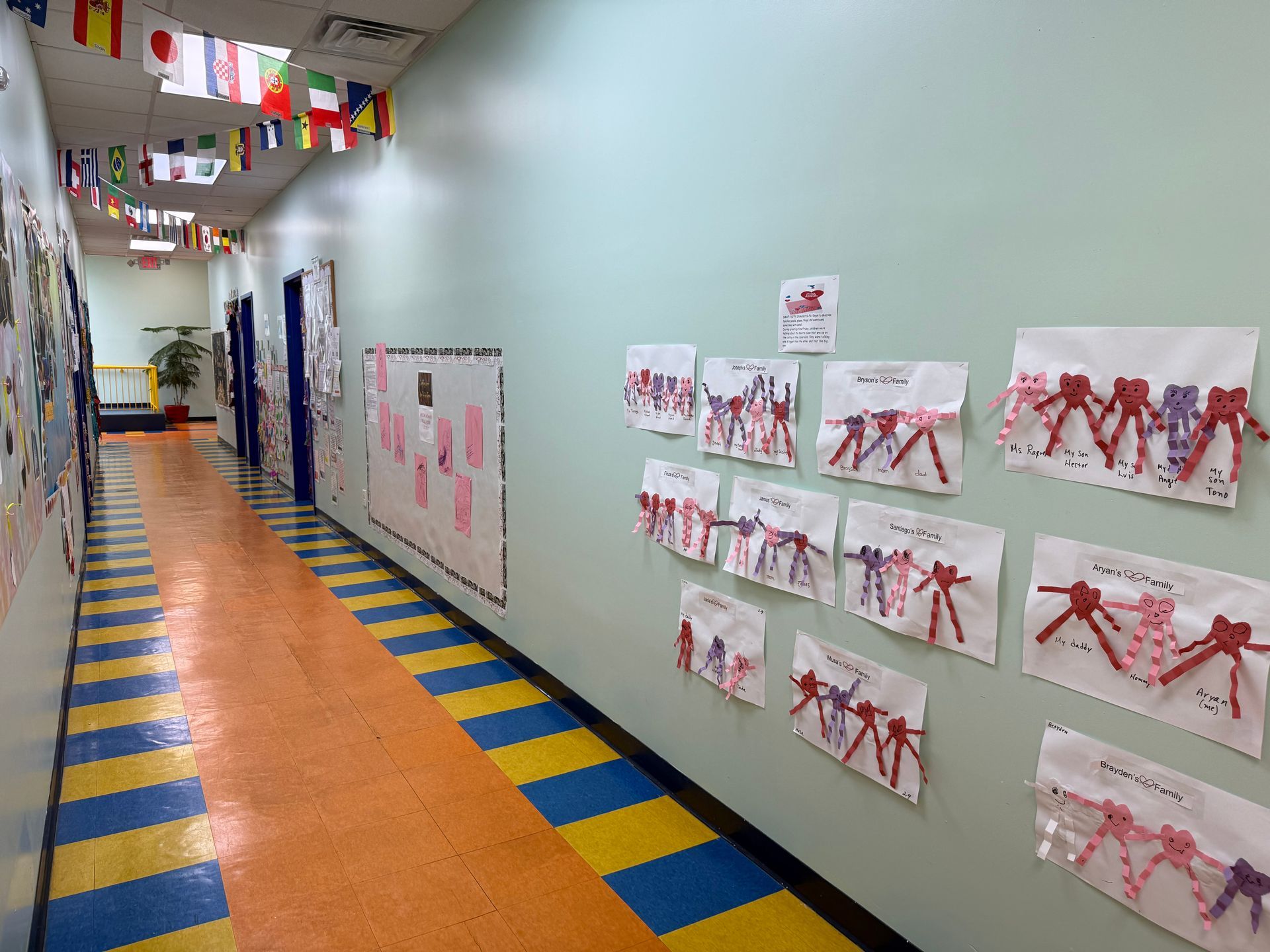 A brightly lit school hallway with a yellow and blue striped floor, adorned with hanging flags and children's art projects.