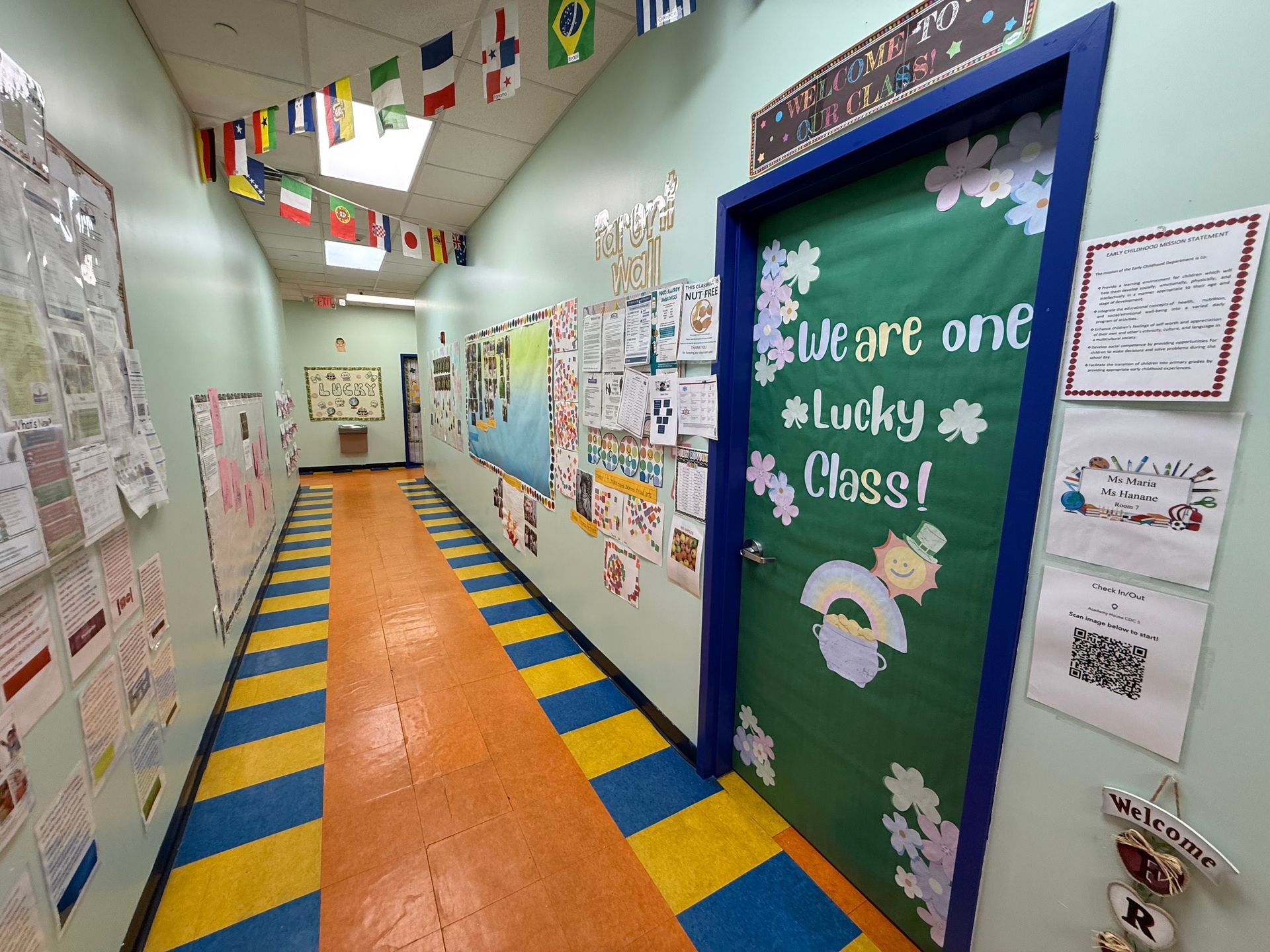 A hallway lined with student work and international flags above, leading to a door labeled 