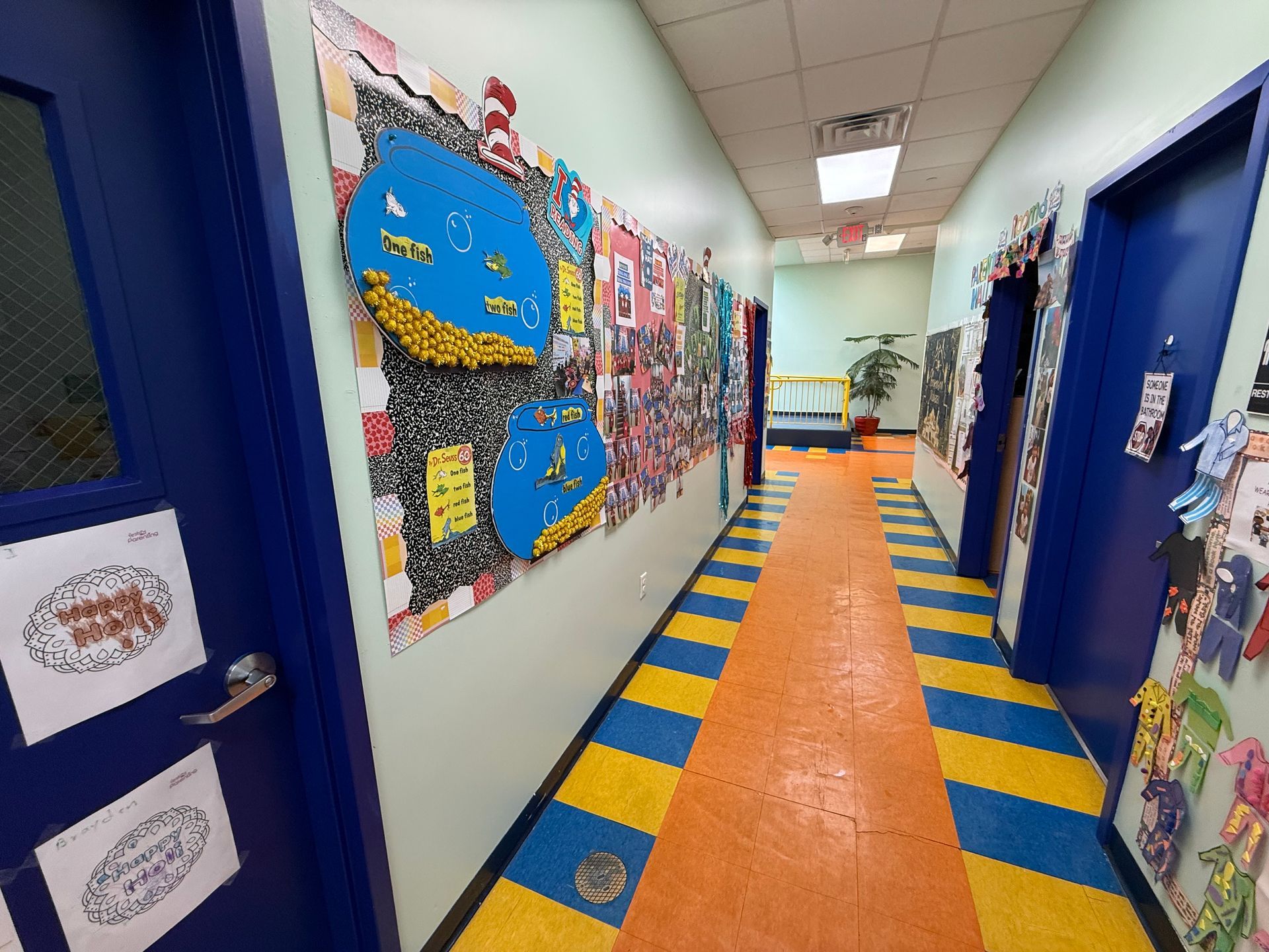 A brightly decorated school hallway with blue doors, colorful wall displays, and an orange and yellow striped floor.