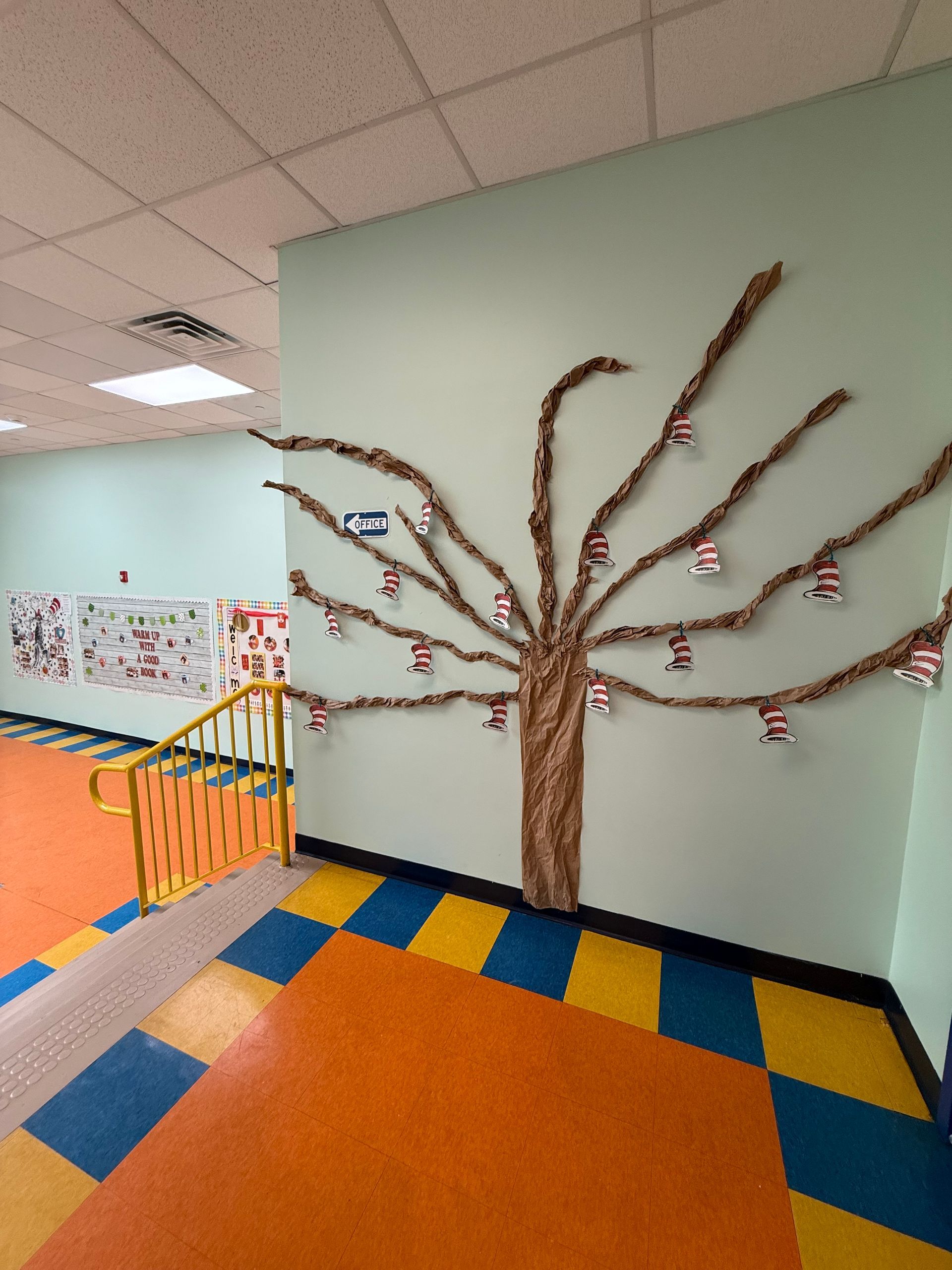 A hallway wall features a brown paper craft tree with Cat in the Hat decorations hanging from its branches.