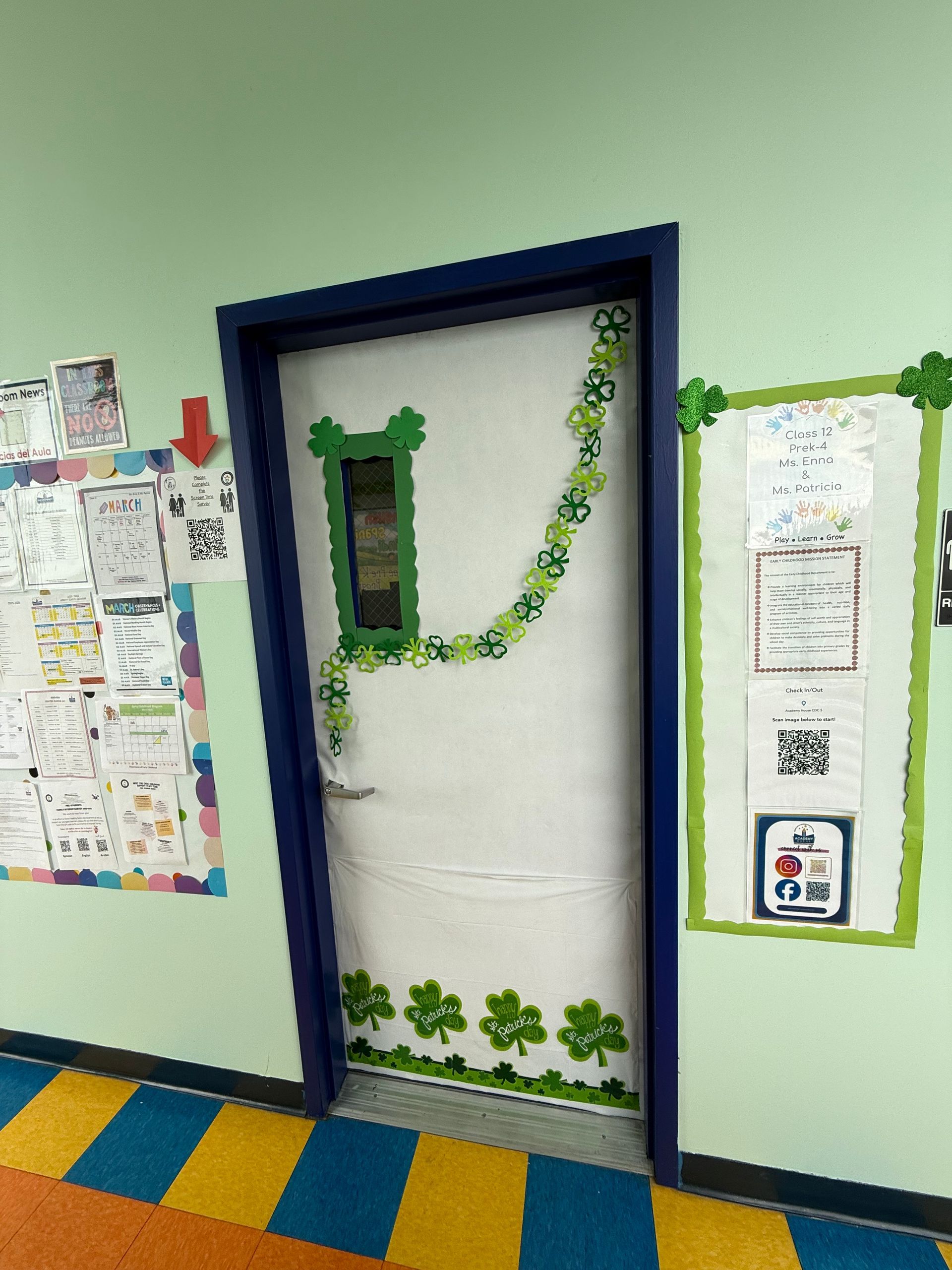 A classroom door decorated for St. Patrick's Day with green shamrocks, set against light green walls and colorful floors.