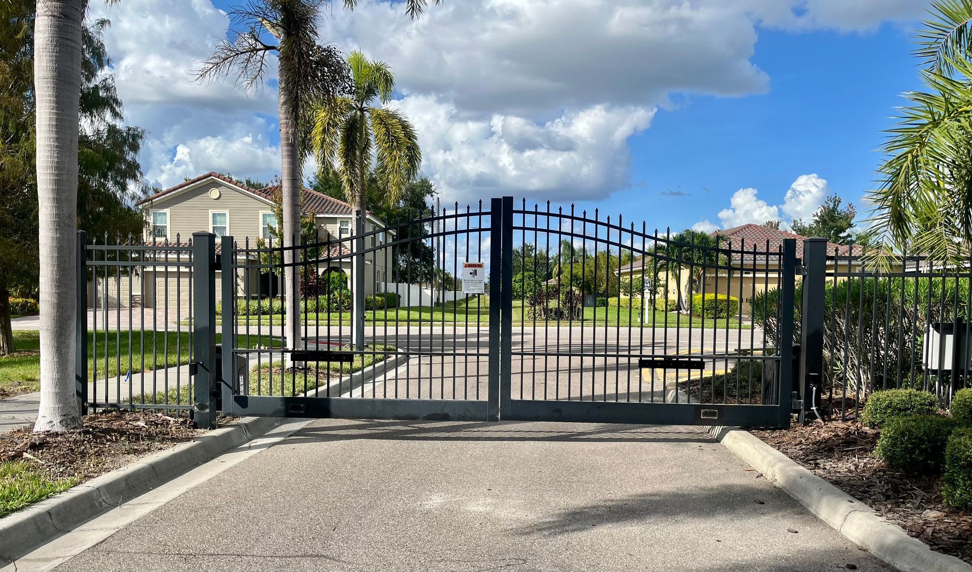 Black gated entrance to a neighborhood with houses in the background