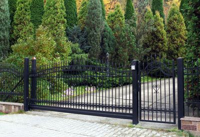 A black sliding gate is open to a driveway surrounded by trees.