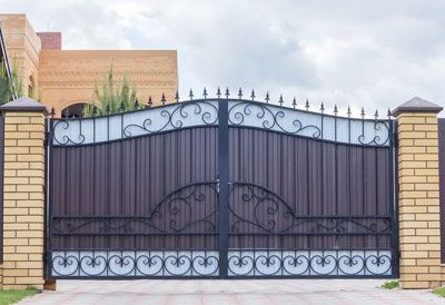 A wrought iron gate with a brick pillar in front of a house.