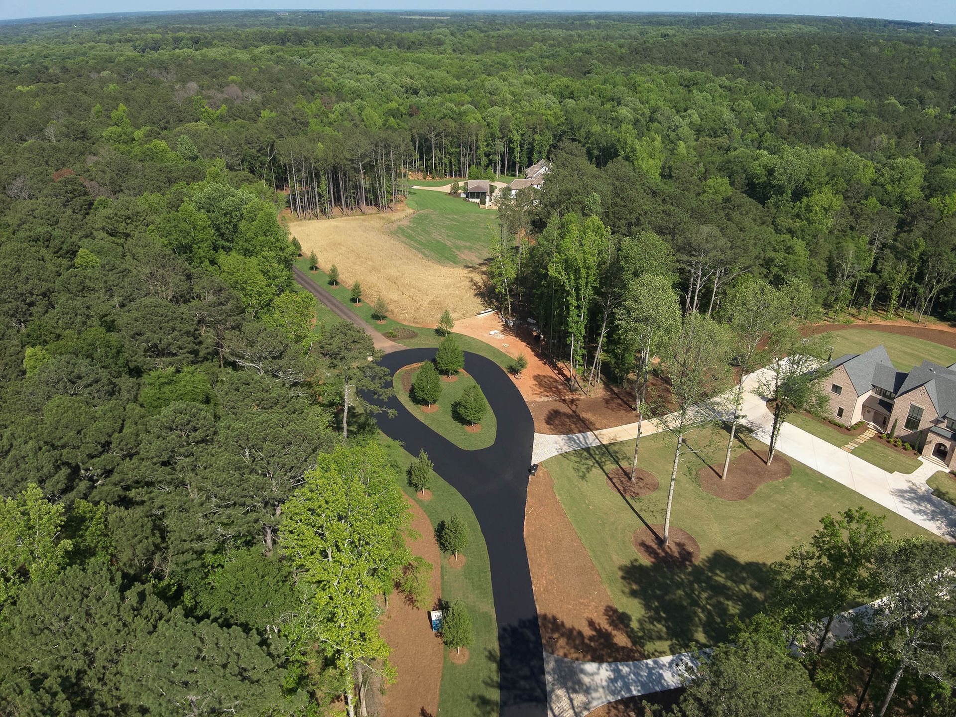 Aerial view of a paved driveway winding through a green wooded area with a house visible.