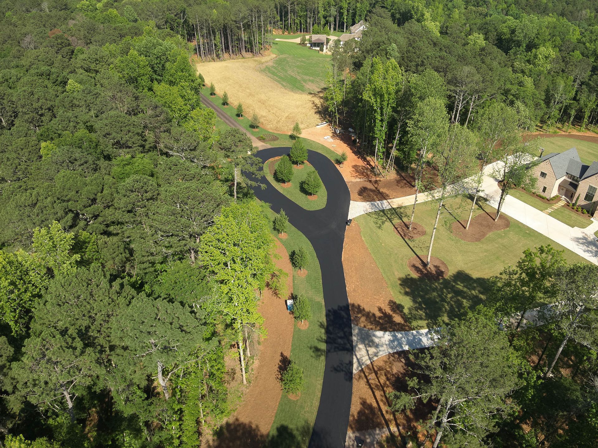 Aerial view of a paved driveway winding through a wooded area to a house.