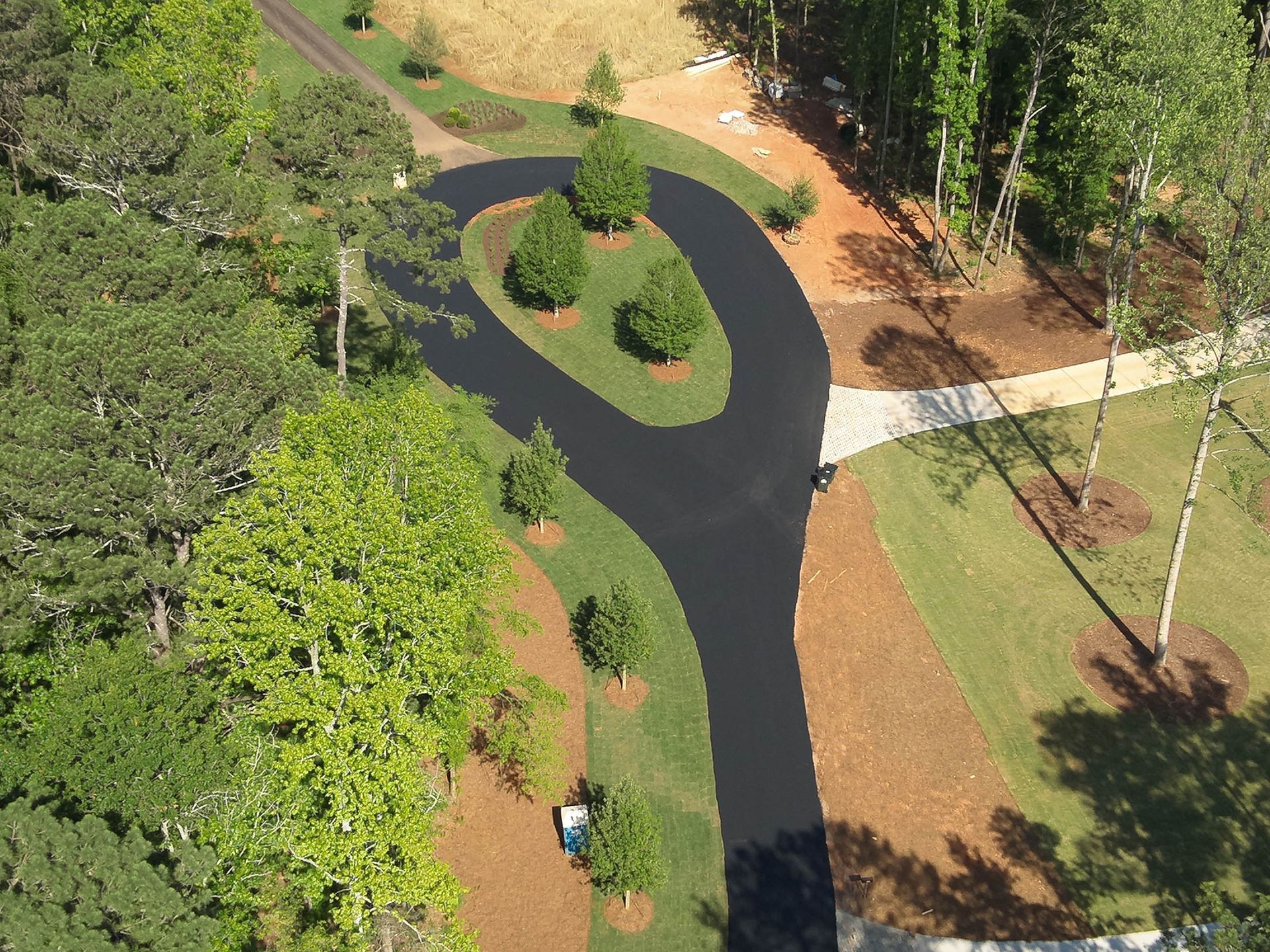 Aerial view: asphalt road winds through green landscaping, trees, and grass.