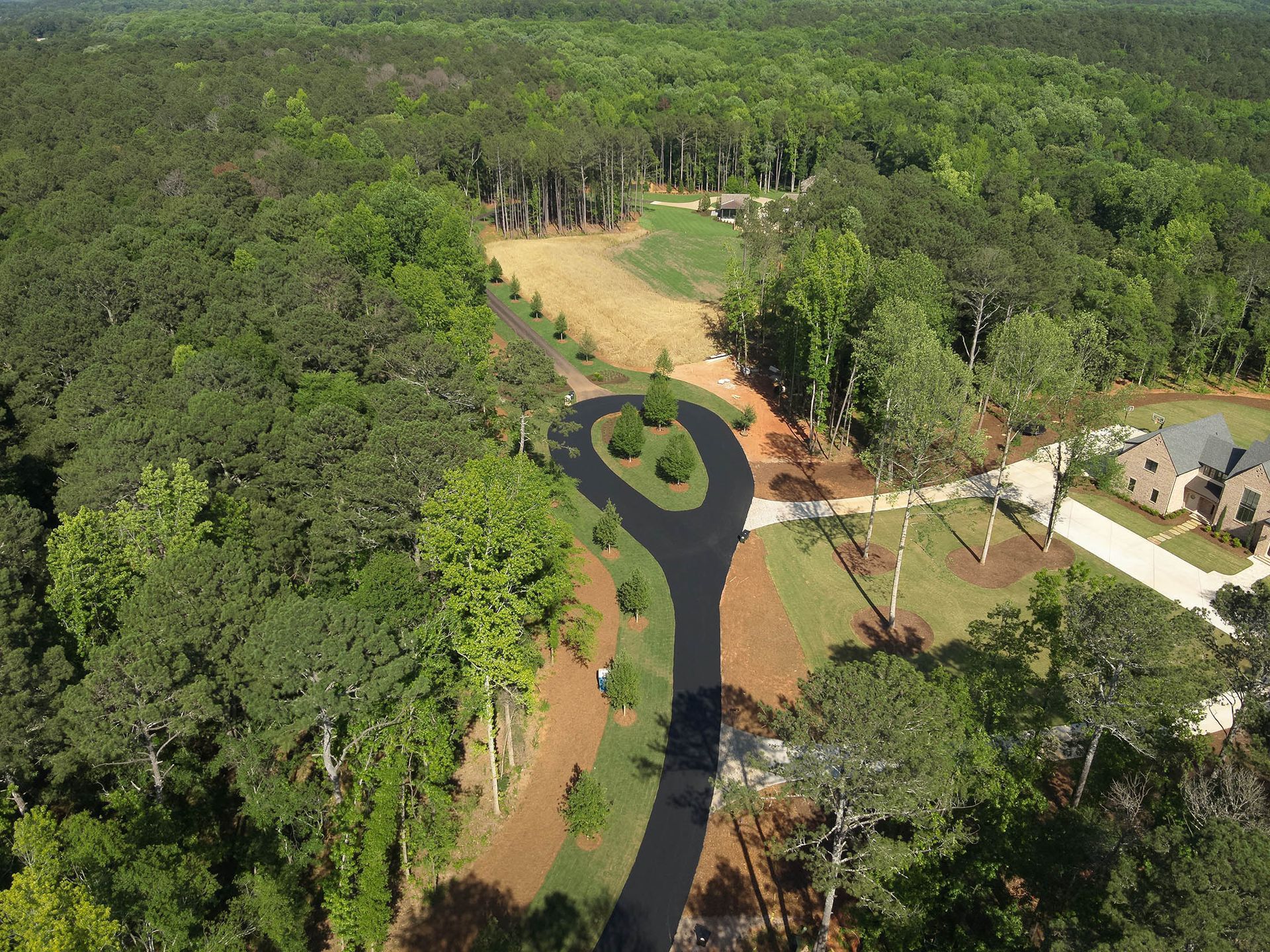 Aerial view of a paved driveway winding through a forest toward a house.