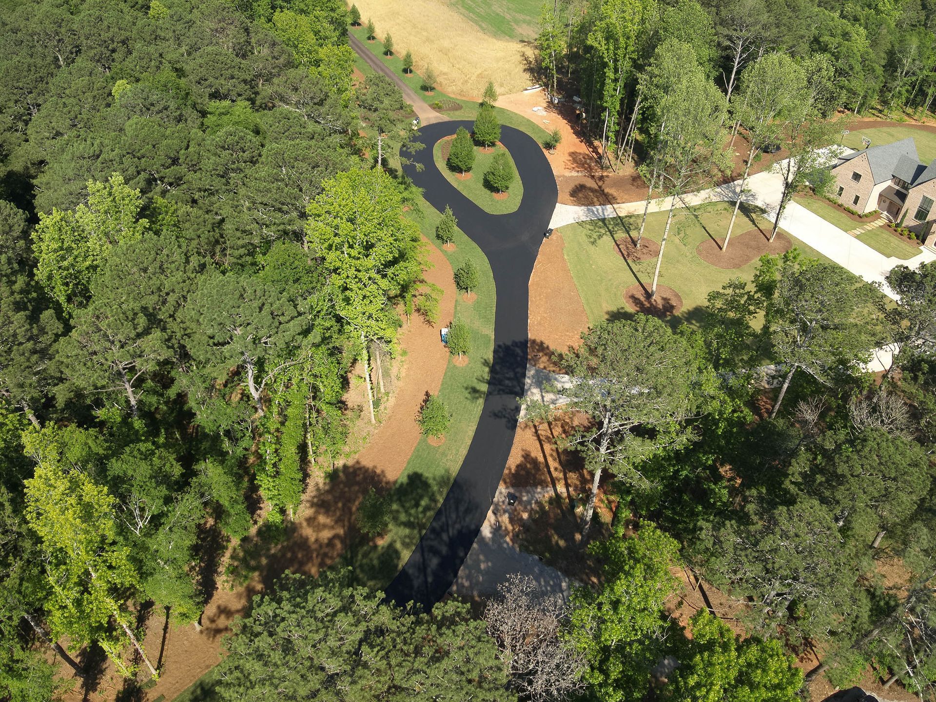 Aerial view of a long, winding asphalt driveway with a circular turnaround in a wooded area, leading to a house.