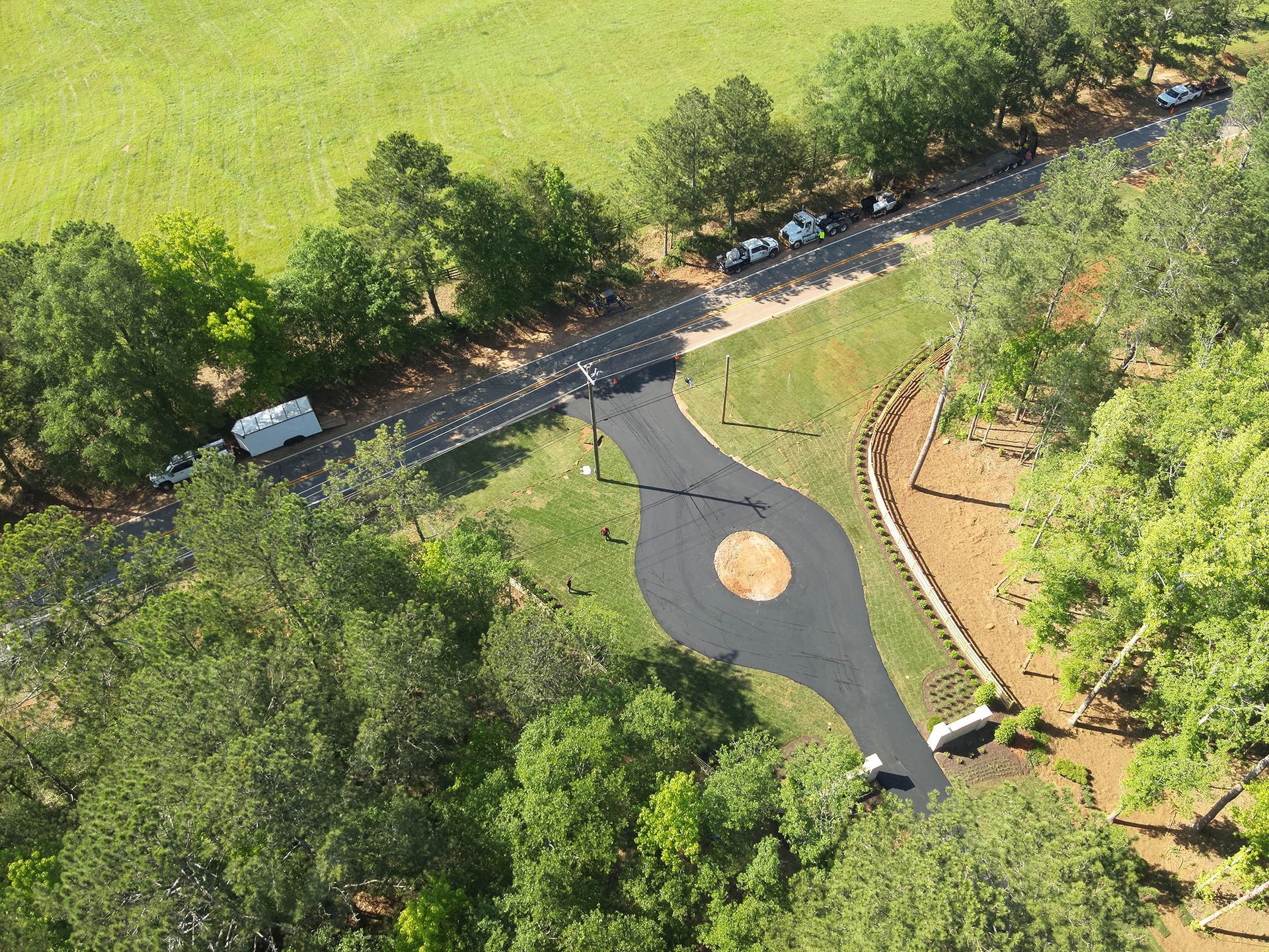 Overhead view of a paved driveway with a central circle and a road in a rural area, with grass and trees.