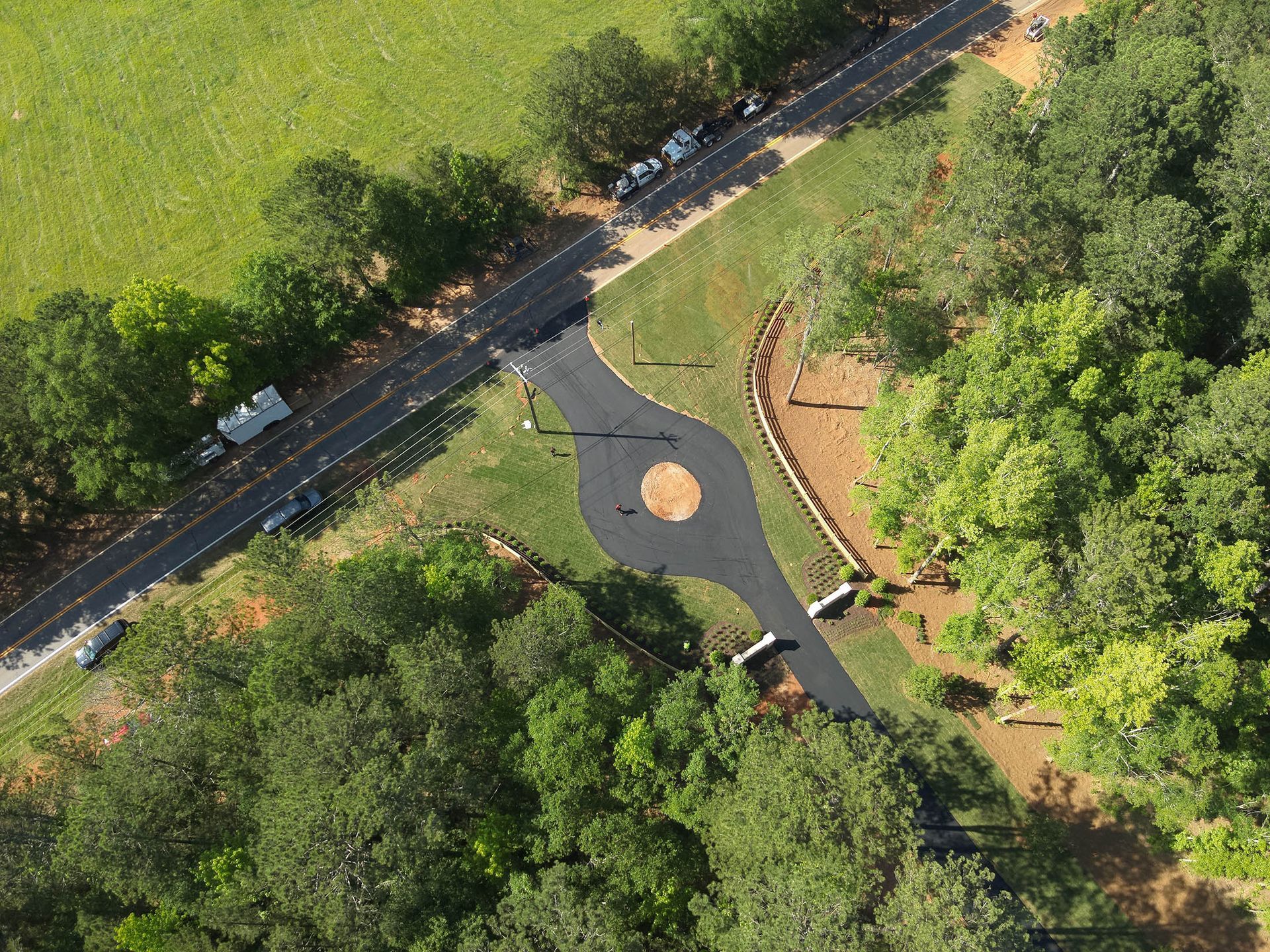 Aerial view of a paved roundabout where roads intersect, surrounded by trees and a grassy field.
