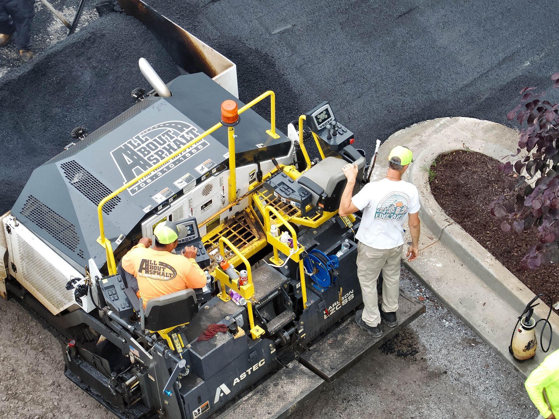 Two men operating asphalt paving machine on a construction site.