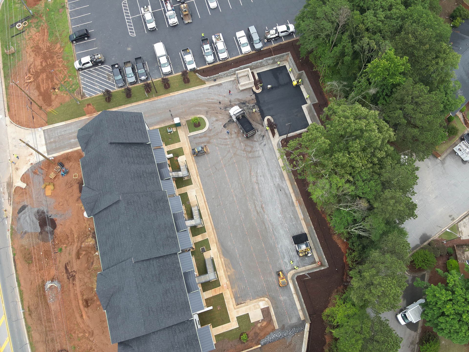 Aerial view of a building with a dark roof and a parking lot being constructed with construction vehicles.