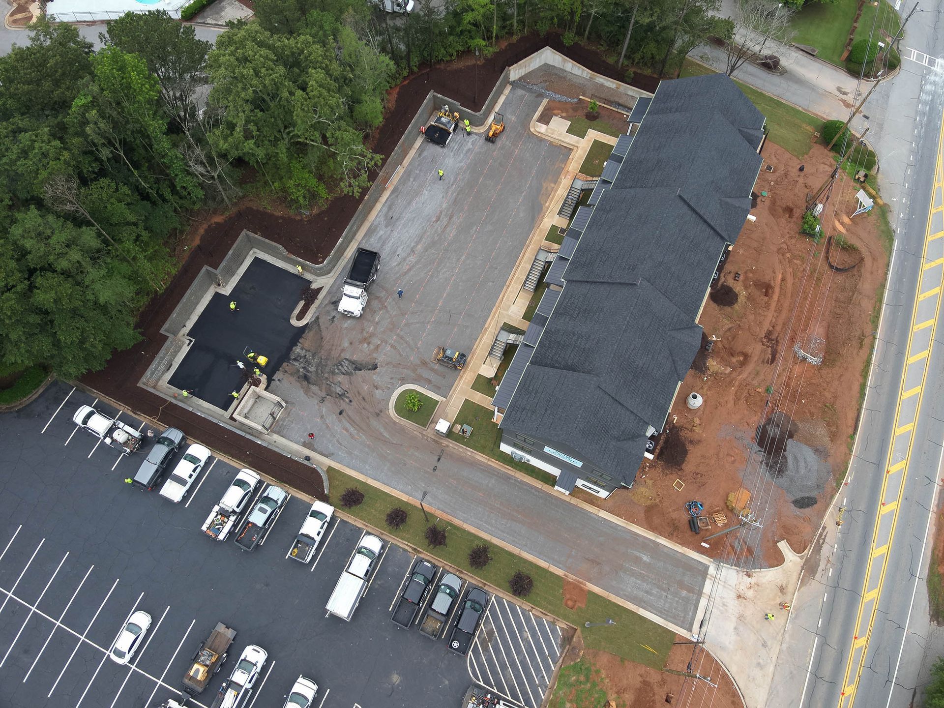 Aerial view of a building under construction, with a large parking lot and surrounding landscaping.