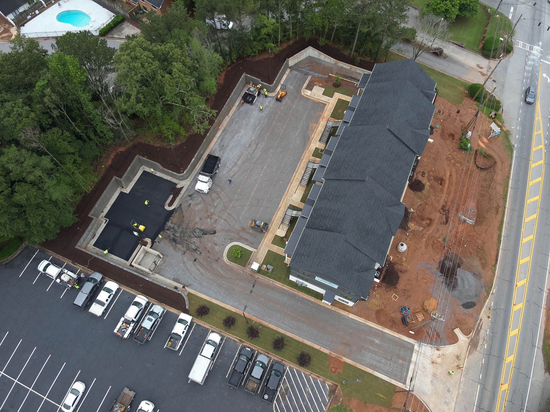 Aerial view of apartment complex under construction with parking, road, and landscaping.