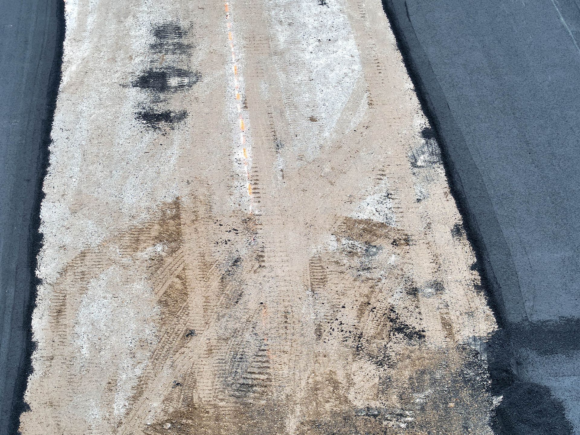 Asphalt road with faded white center markings, covered in sand and debris.