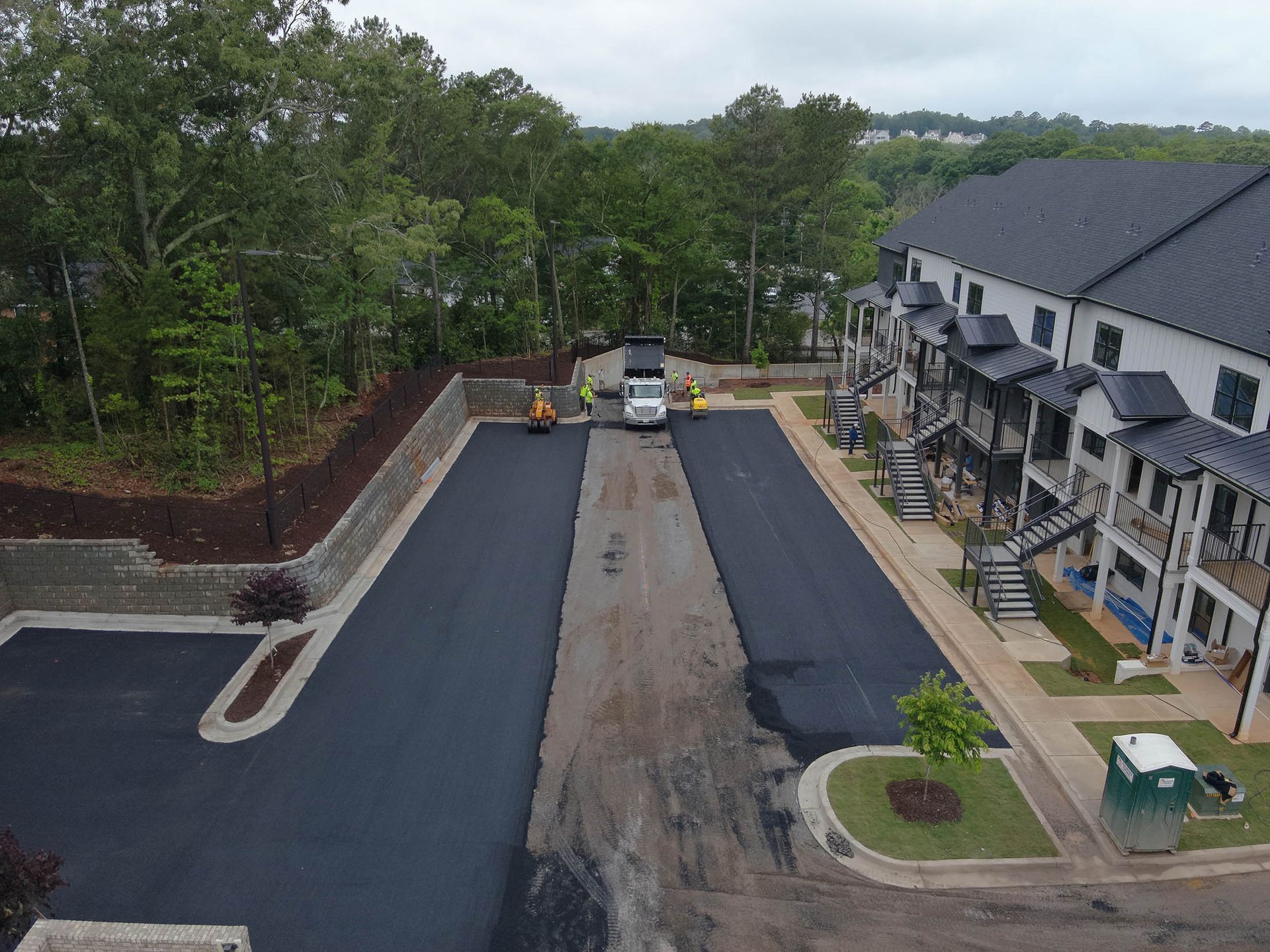 Asphalt paving a road in front of apartments. Workers and equipment are visible.