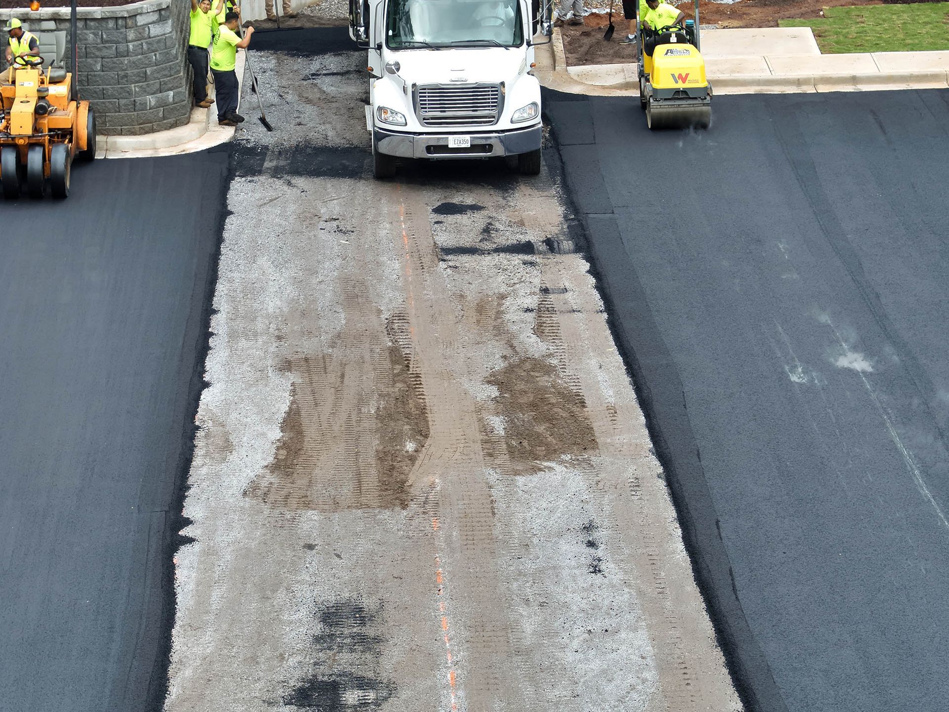 Asphalt paving work with truck, workers, rollers compacting fresh black asphalt.