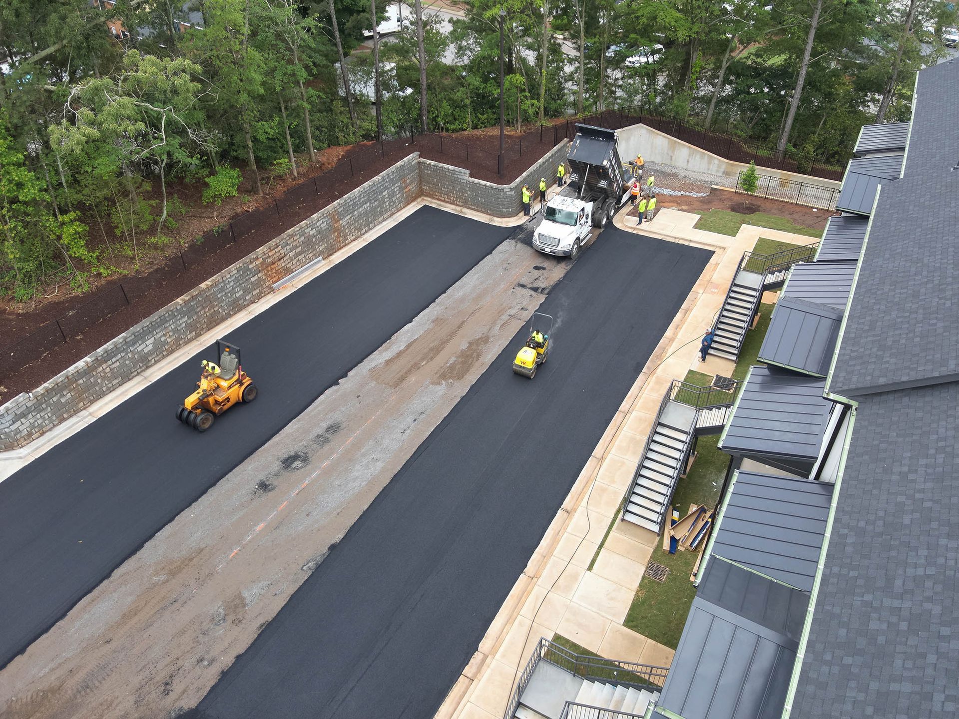Asphalt paving in progress on a parking lot, with workers, trucks, and equipment.