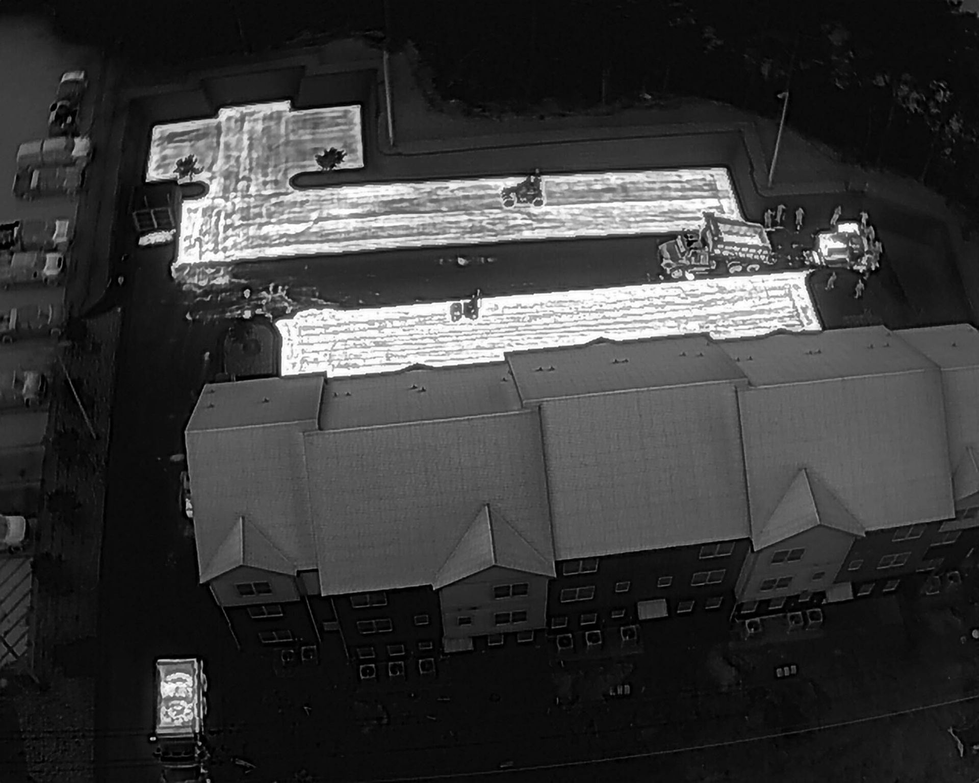 Aerial view of a building under construction, with completed apartments and parked cars visible.