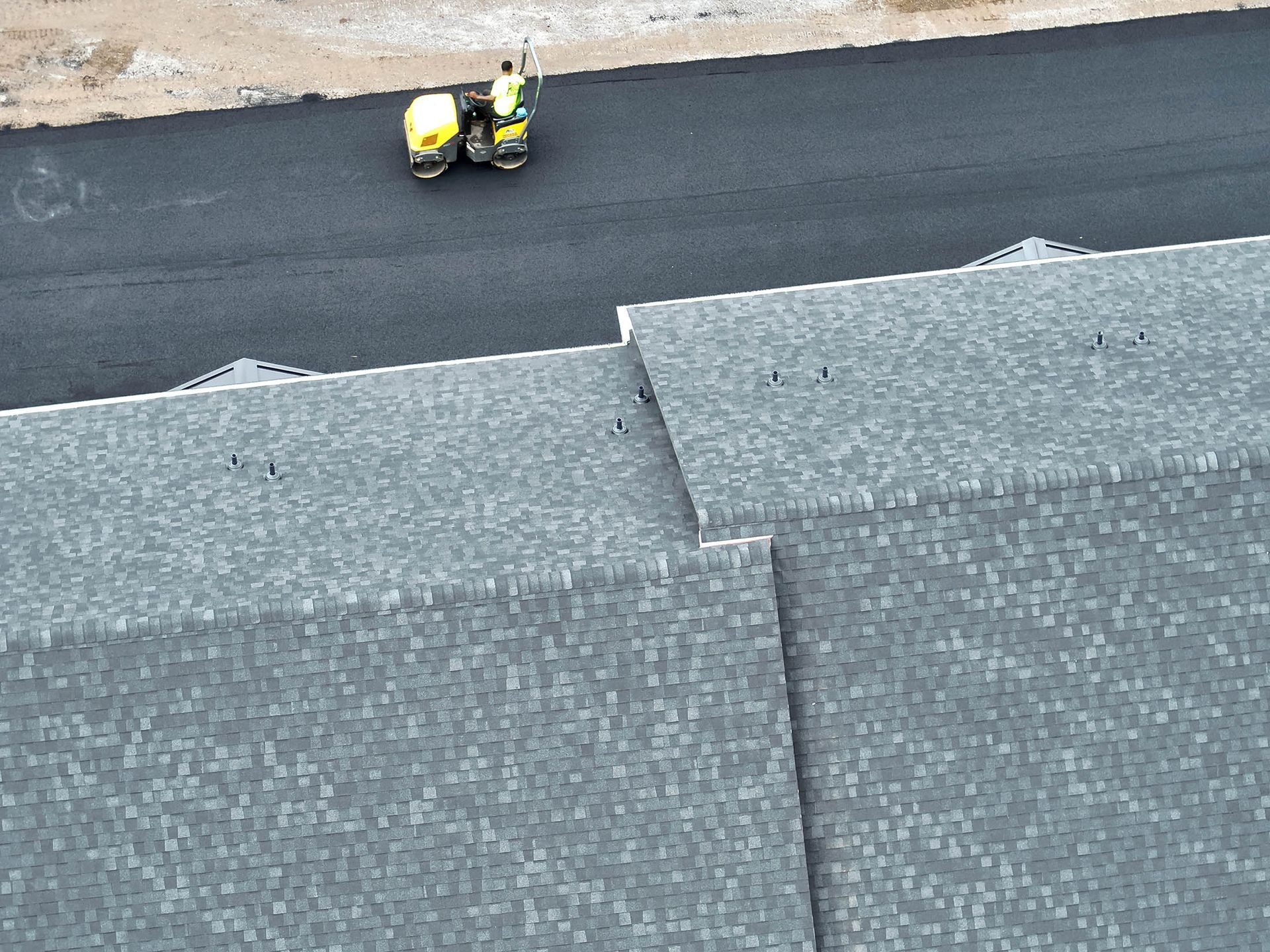Gray asphalt shingles on a roof with road work happening in the background.