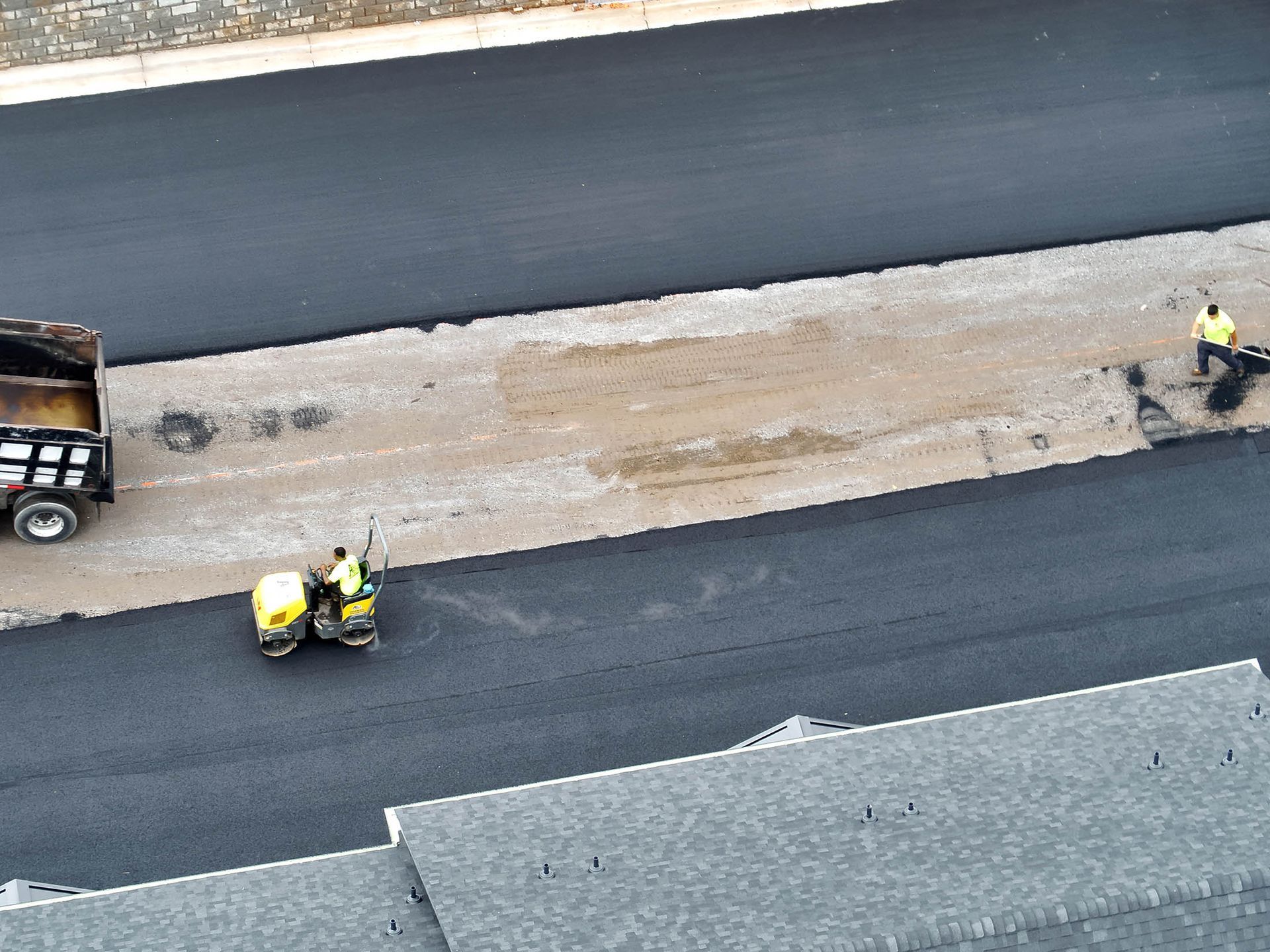 Road construction with workers laying asphalt on a street. A truck and roller are visible.