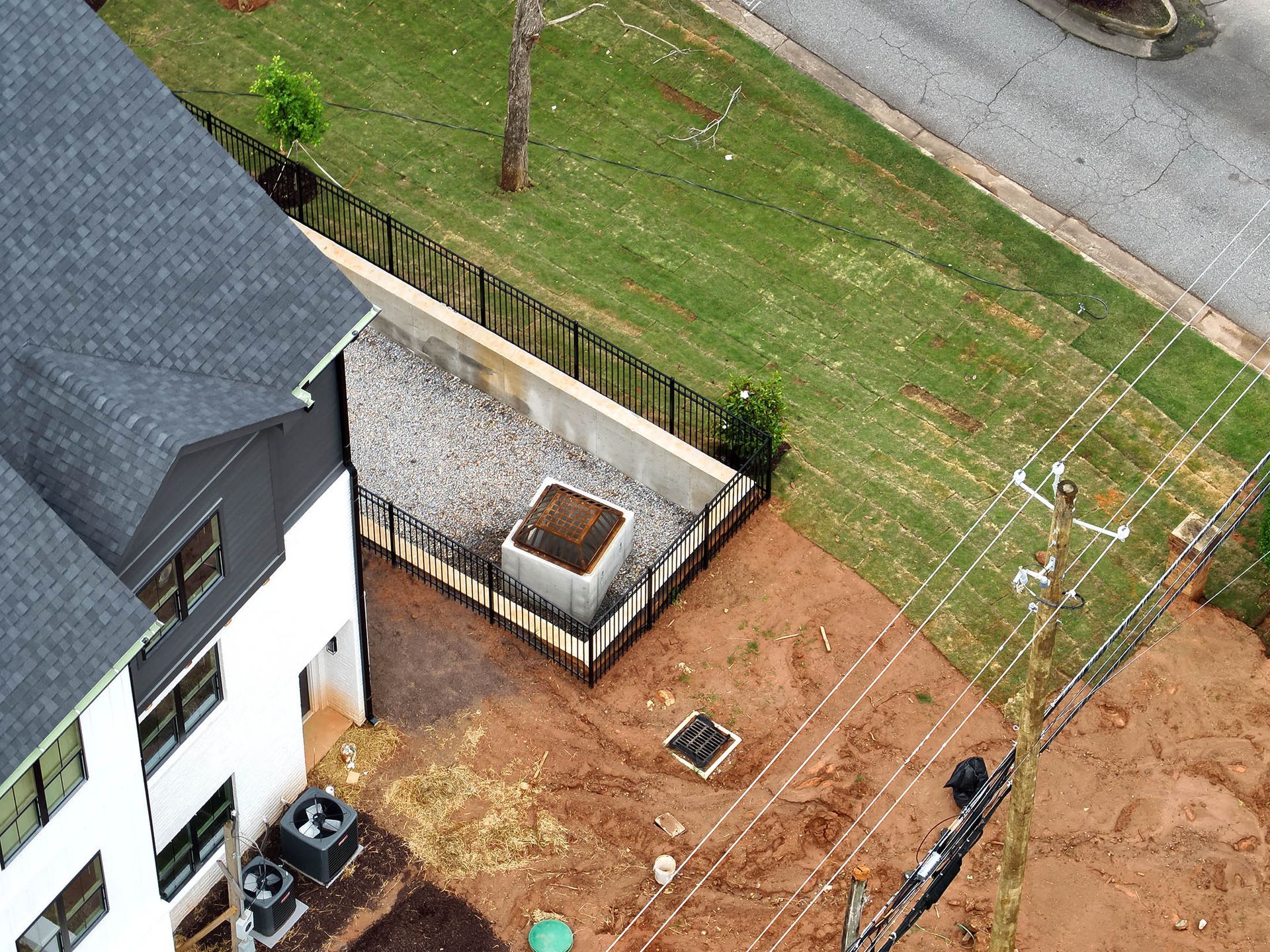 Aerial view of a house and yard with power lines, grass, and a gravel area.
