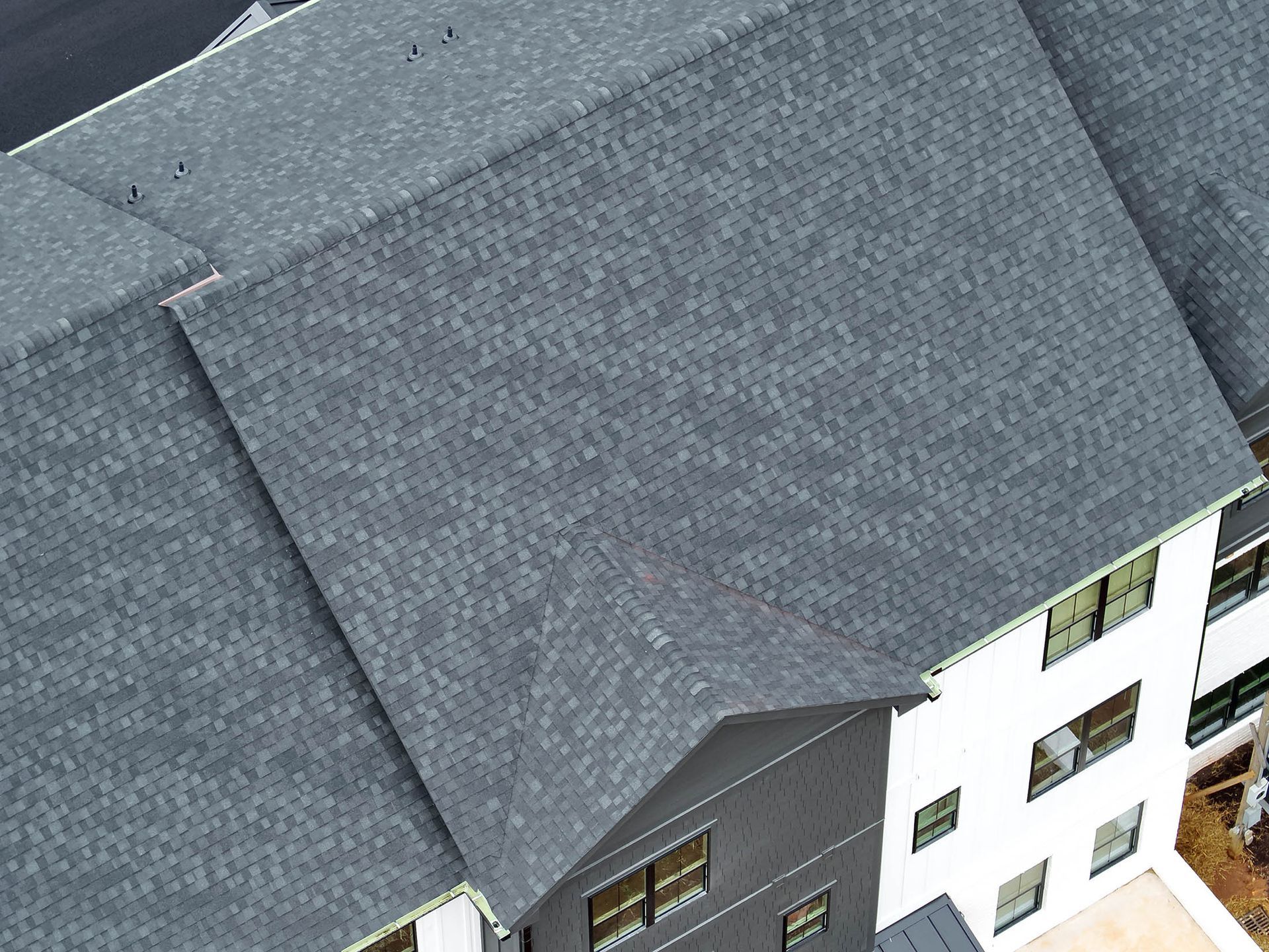 Overhead view of a building with a dark gray shingle roof and white and gray exterior walls.