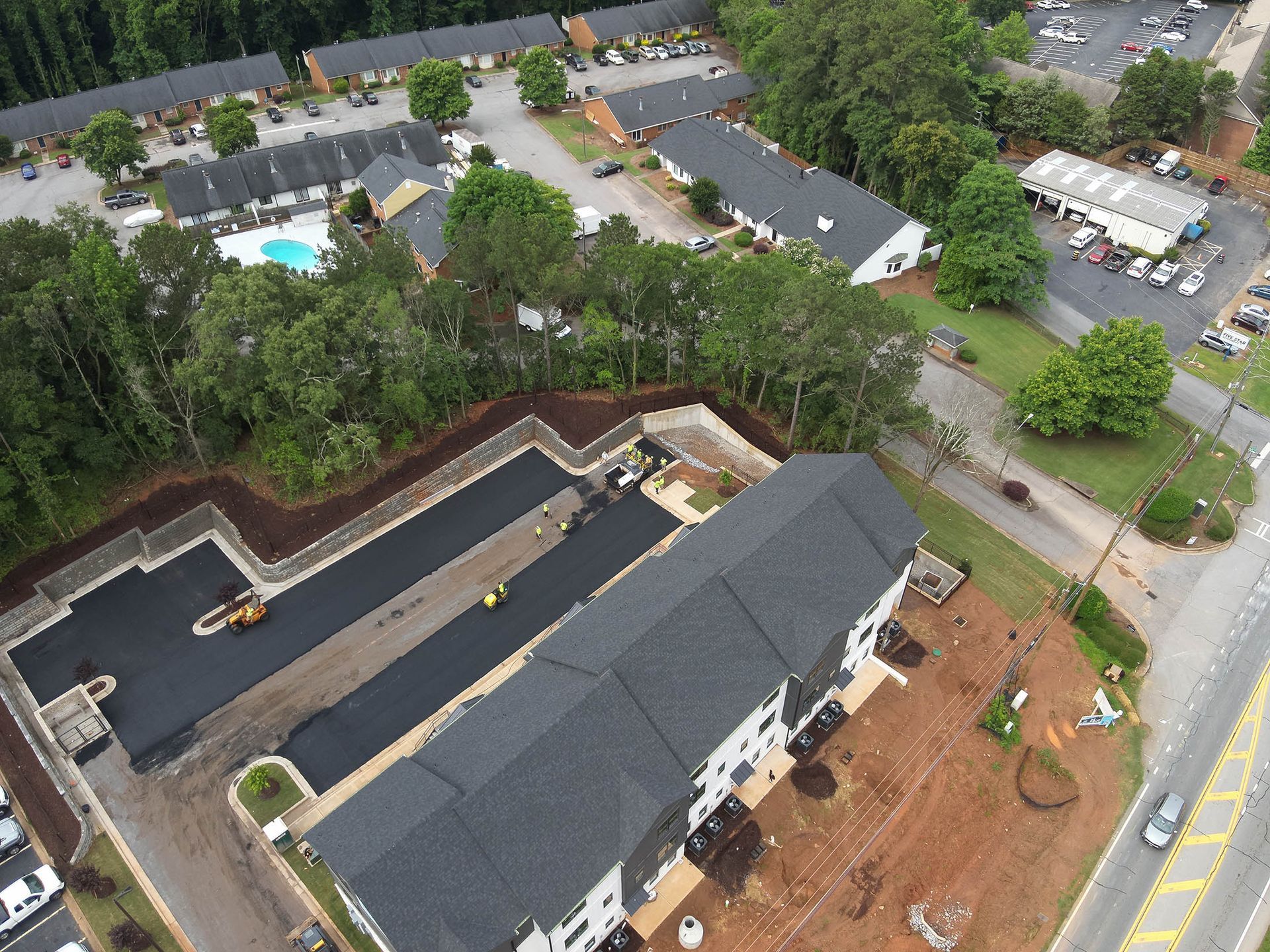 Aerial view of construction site with asphalt paving, workers, and apartment buildings.