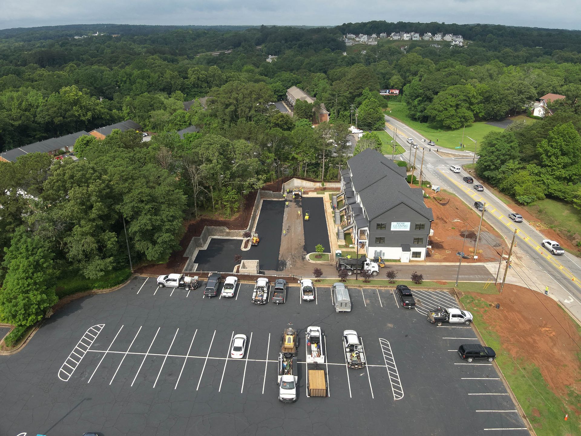 Aerial view of new asphalt parking lot and building construction next to a busy road.