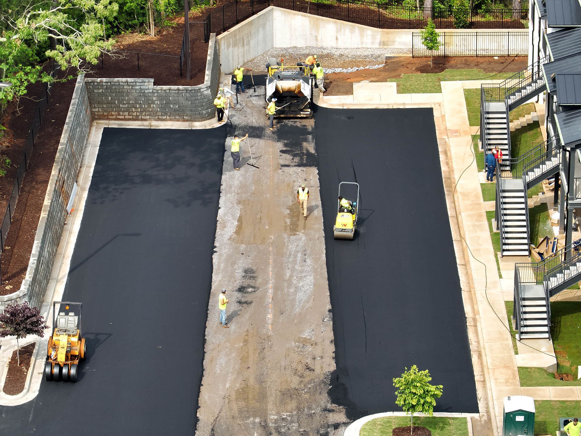 Asphalt paving of a parking area. Workers and machinery compacting the surface.