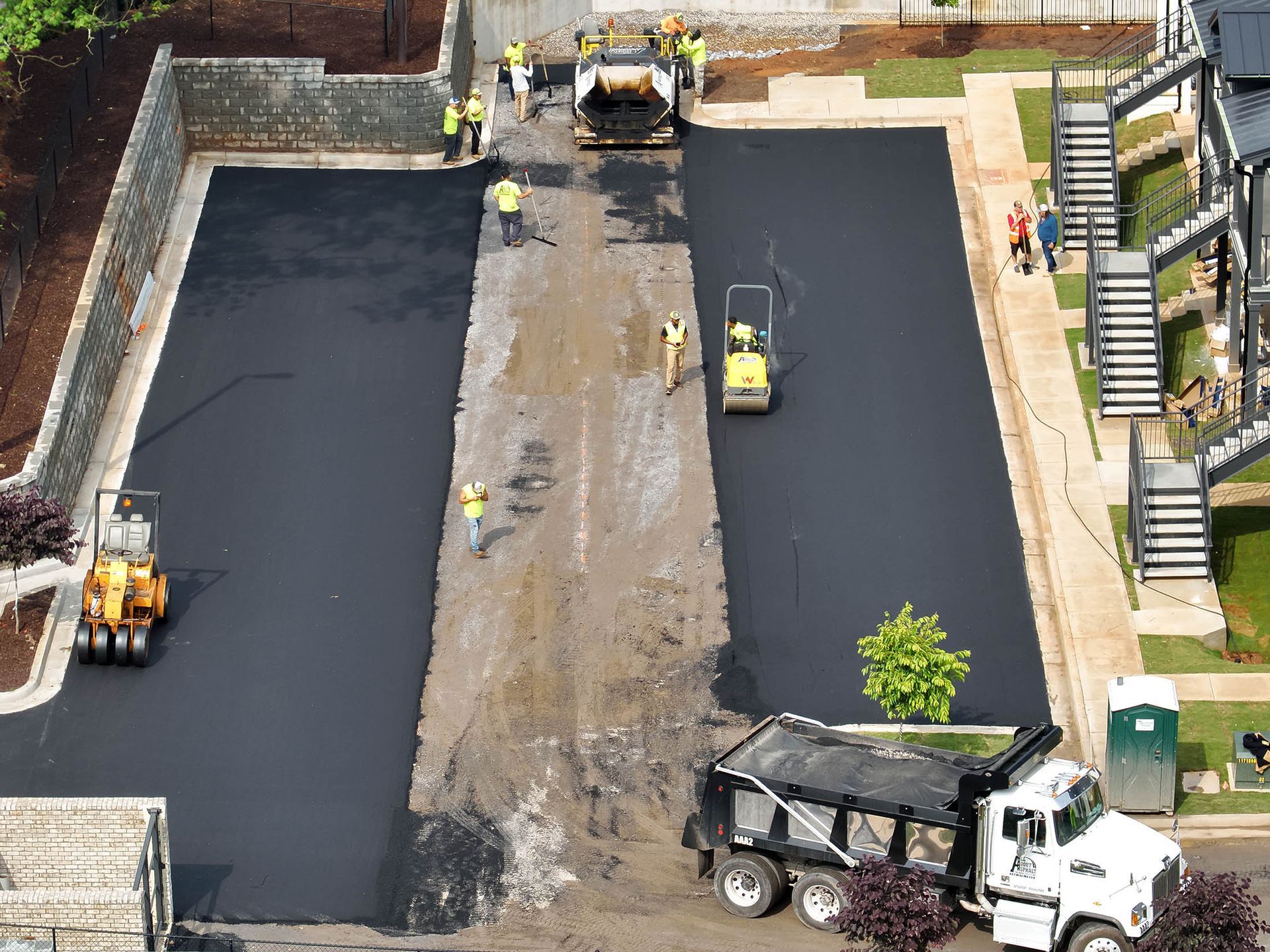 Asphalt paving of a parking area by construction workers and machinery.