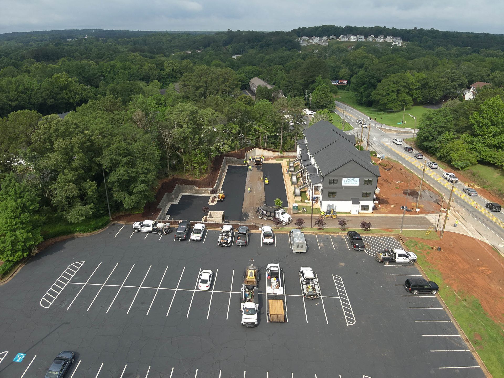 Aerial view of a parking lot and a newly constructed building next to a road, construction equipment present.