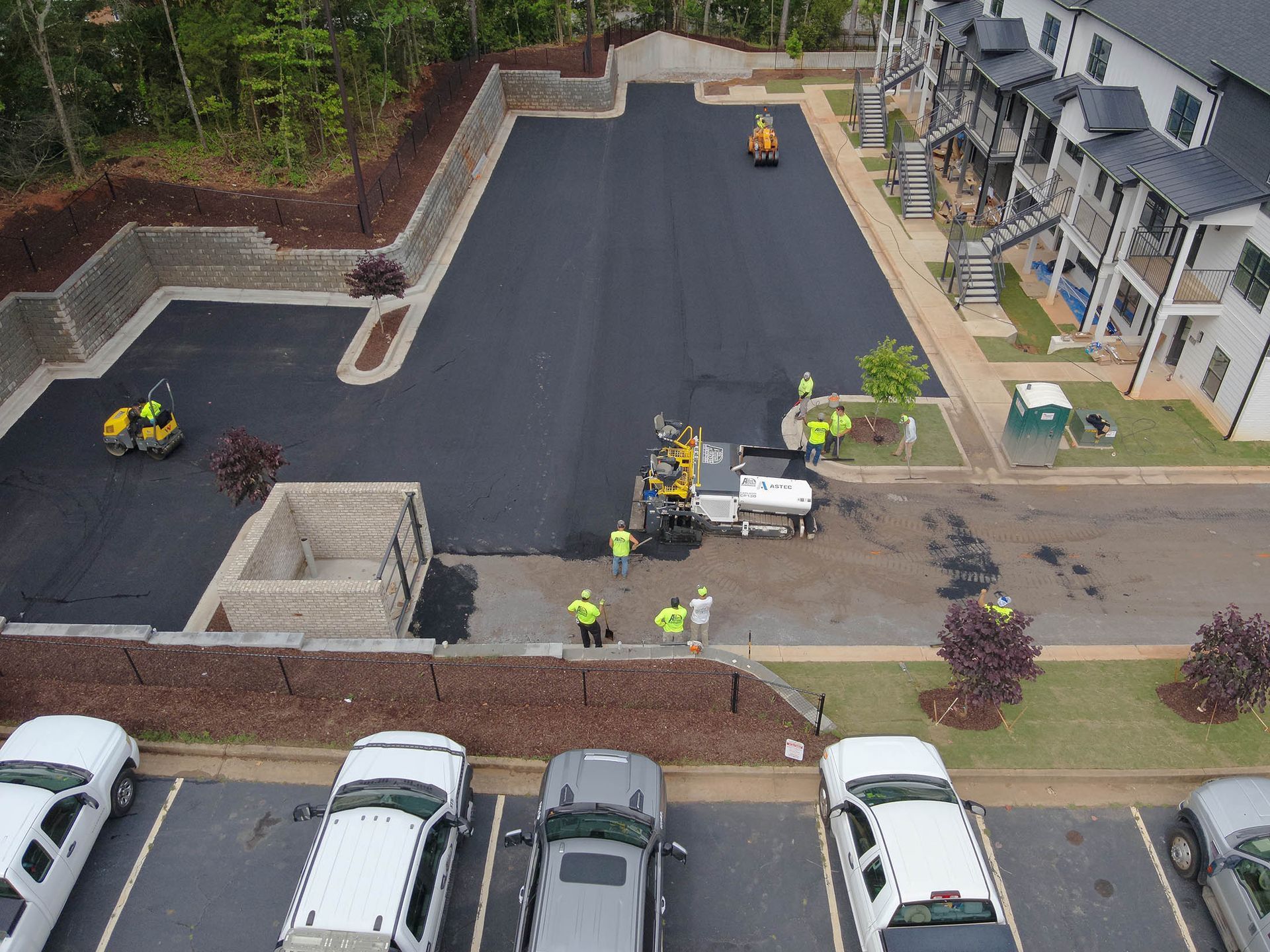 Asphalt paving project. Workers and machines laying asphalt in a parking lot next to an apartment building.