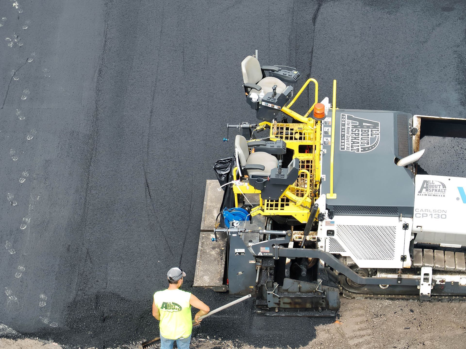 Asphalt paving machine laying blacktop with worker in safety vest.