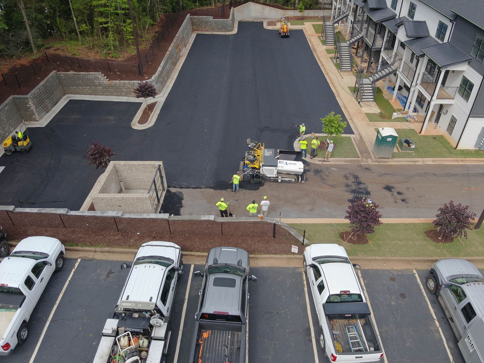 Asphalt paving construction in parking lot with workers and trucks.