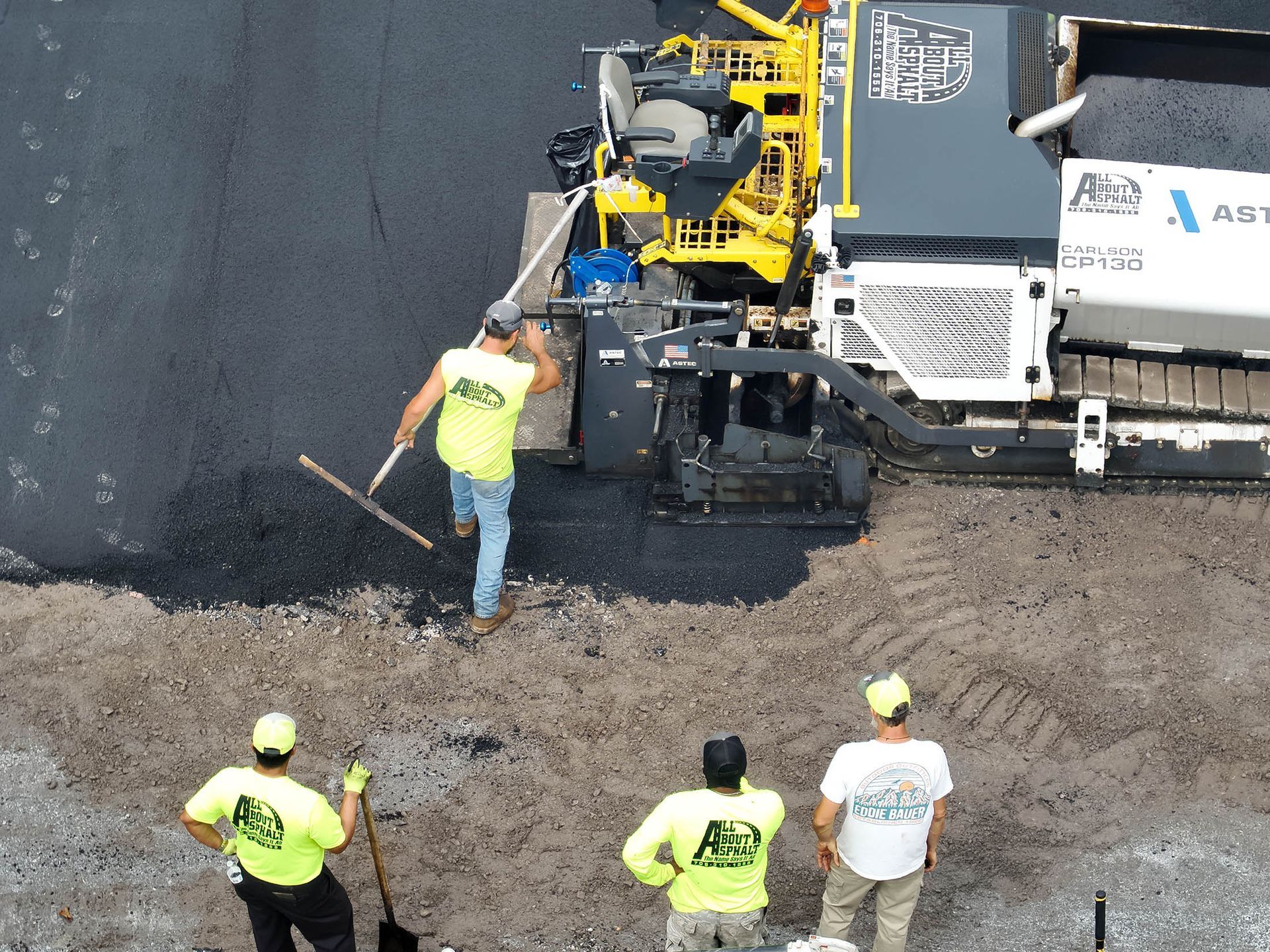 Road construction crew paving asphalt. Yellow safety vests, machine, and workers.