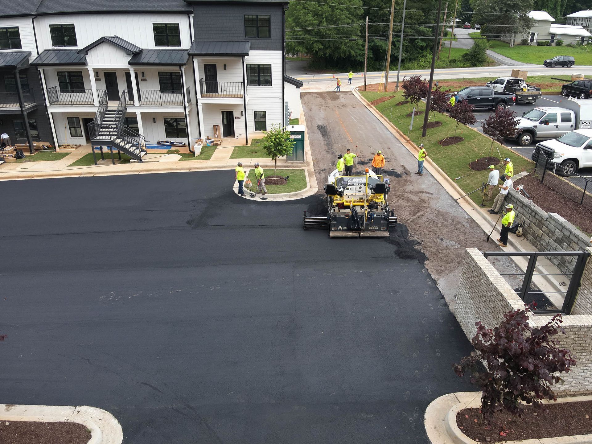 Paving crew laying asphalt on a road and parking lot near new townhouses.