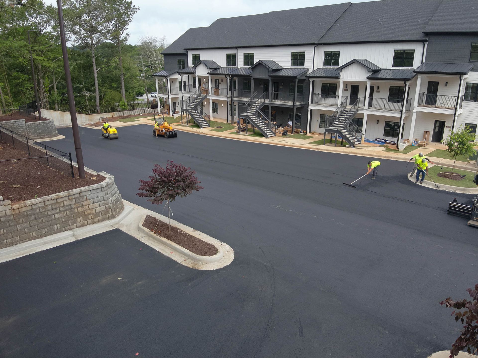 Asphalt paving crew at work, laying blacktop for a parking lot near multi-story white building.