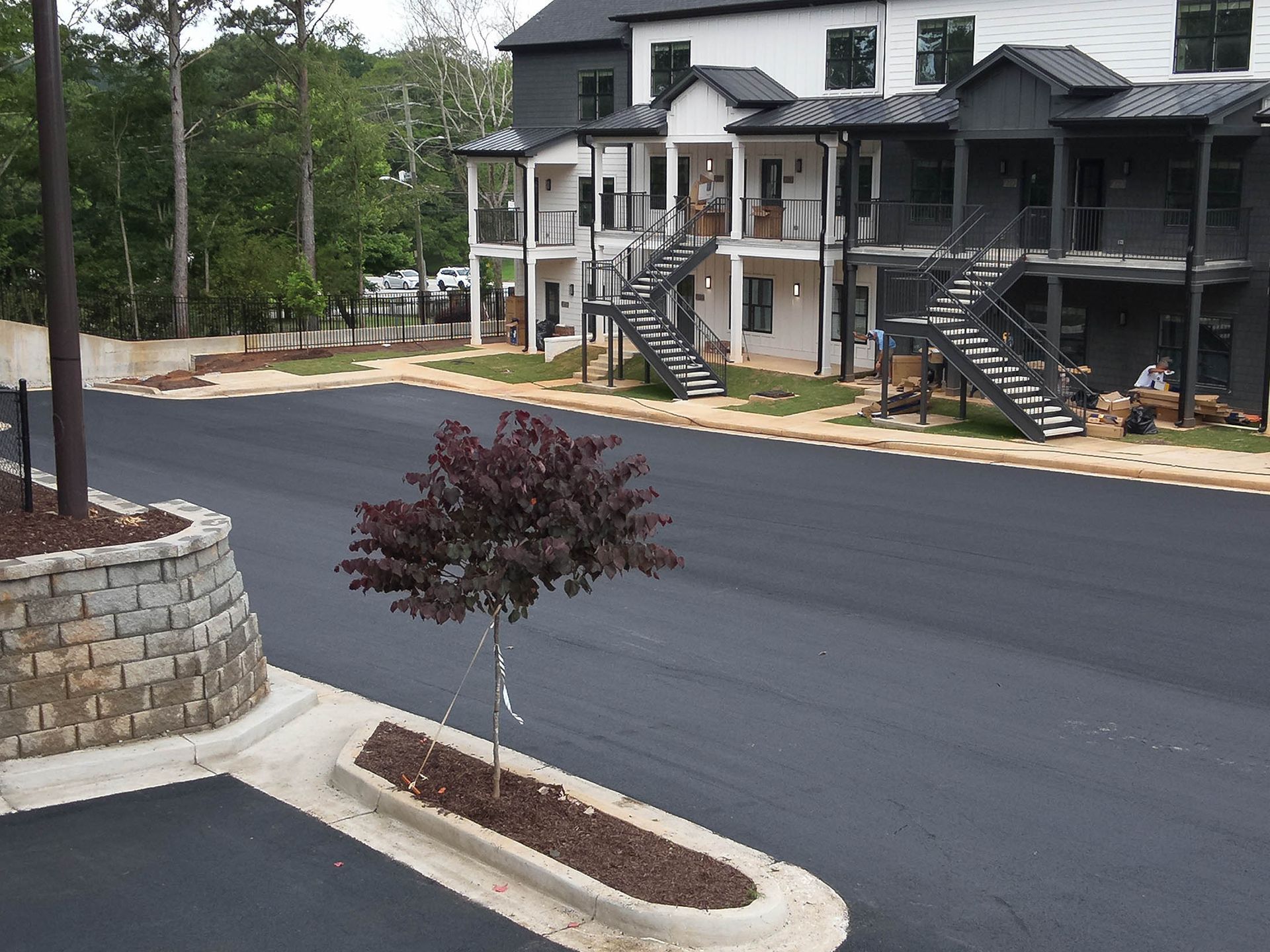 Apartment building with exterior staircases and asphalt parking lot, a tree in the foreground.