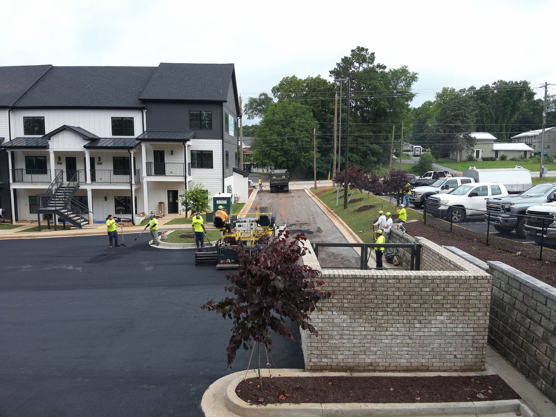 Construction workers paving a parking lot near a multi-story apartment building.