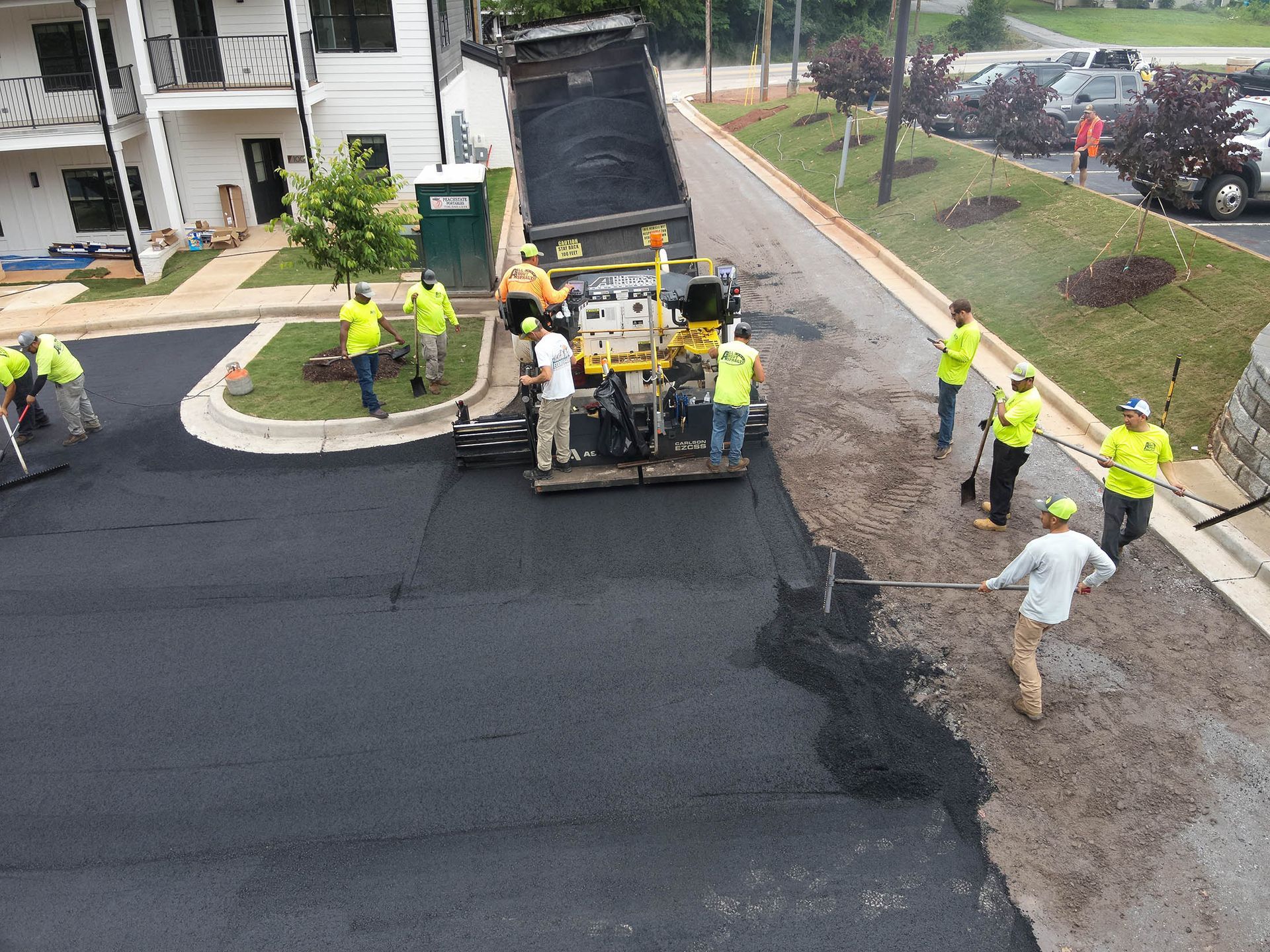 Construction crew paving asphalt road. Dump truck unloading. Workers in yellow vests.