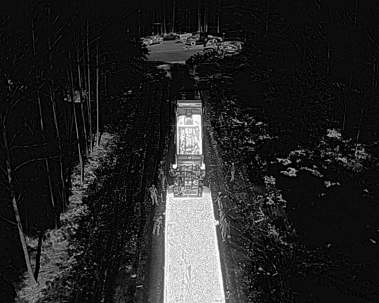 Overhead grayscale view of a truck driving on a dark road through a forest.