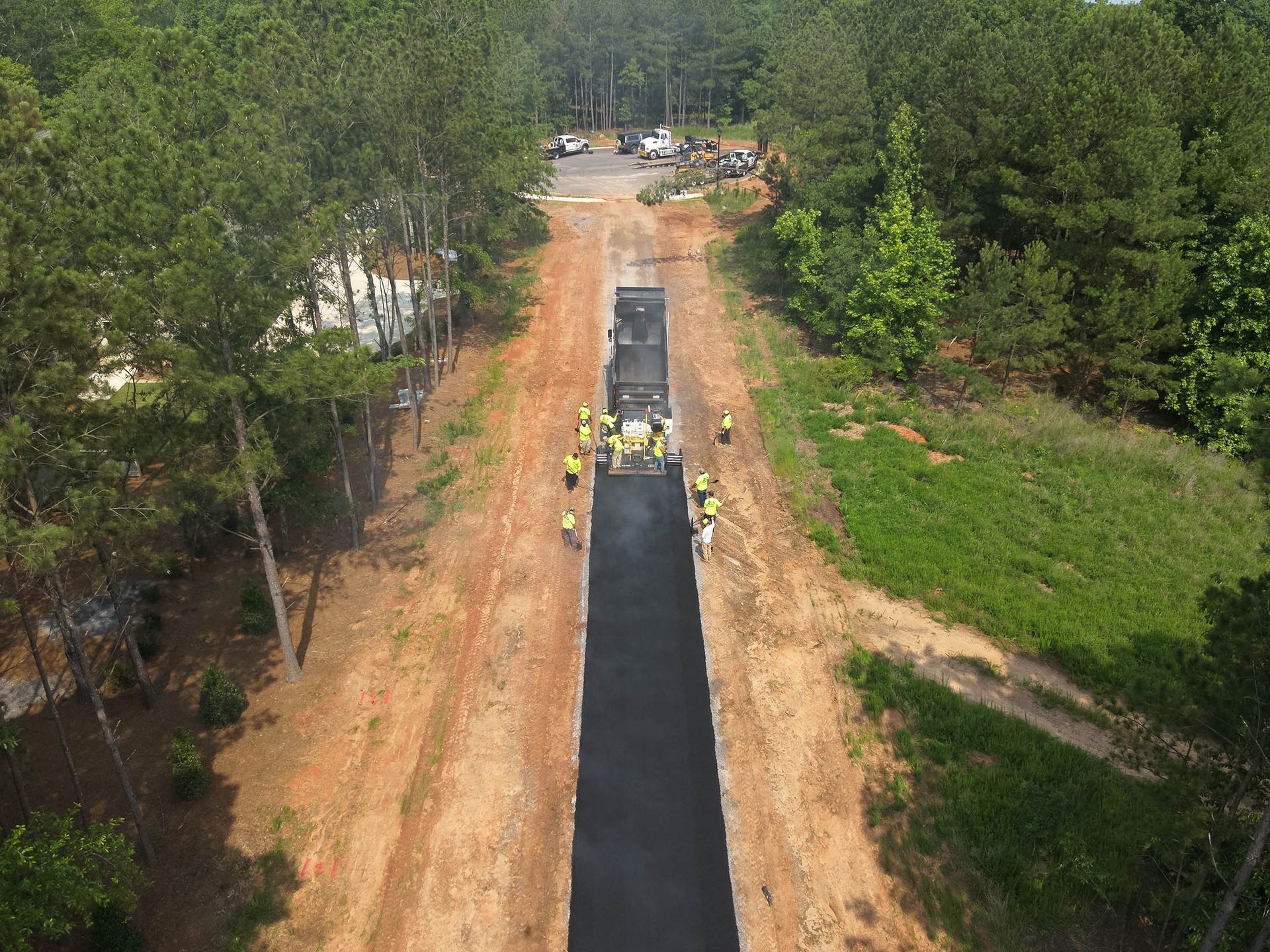 Road construction. Asphalt paving on a wooded road, several workers and machinery present.